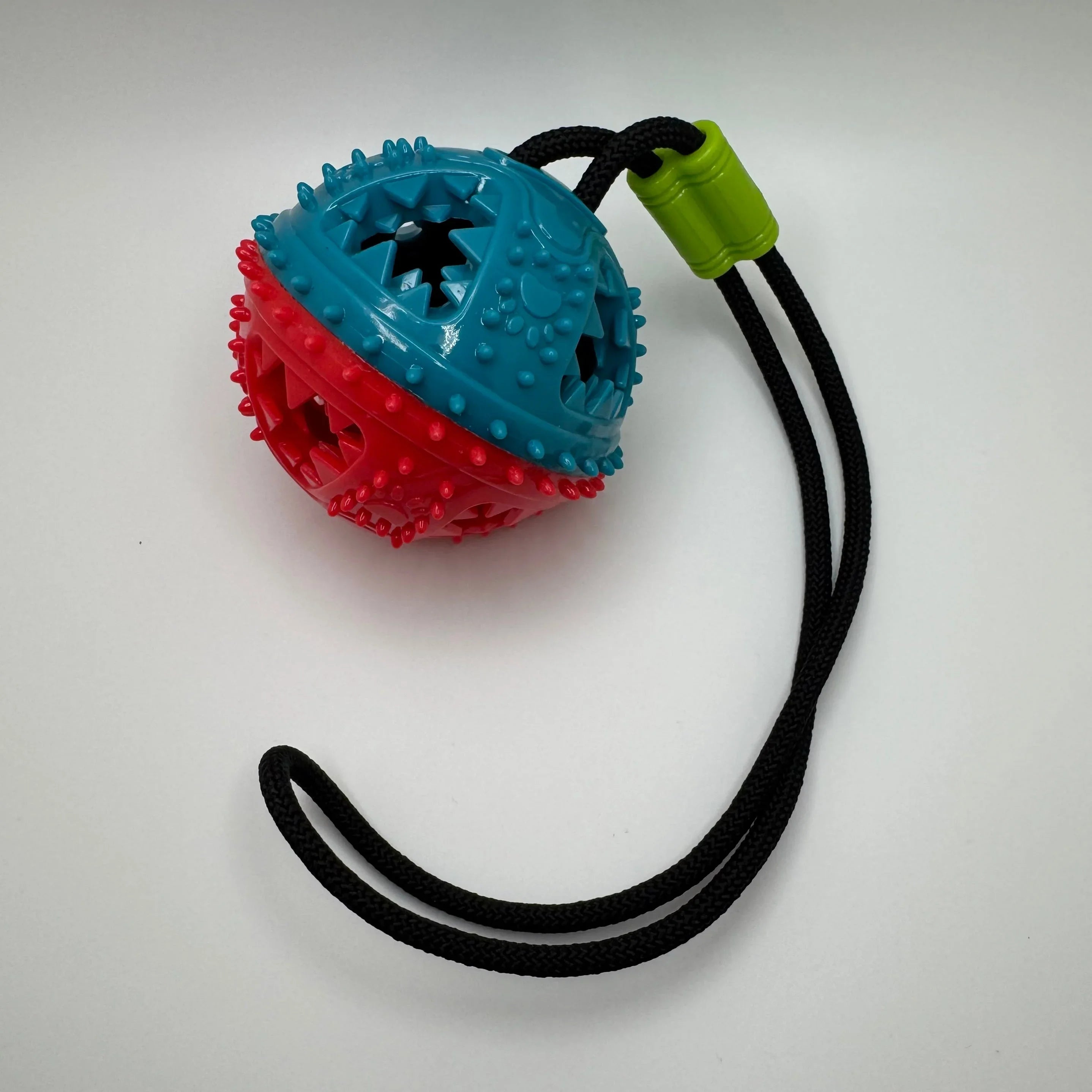 Blue and red spiked dog chew ball toy with black rope handle on white background