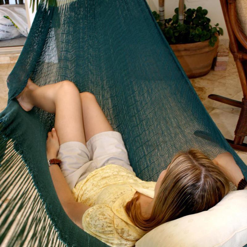 Woman relaxing in a forest green Mayan hammock indoors with plants and wicker furniture