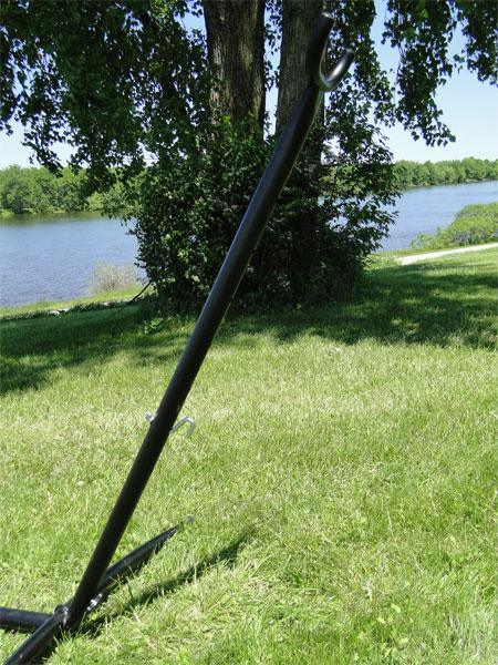 Black universal hammock stand on green grass near trees and a lake outdoors