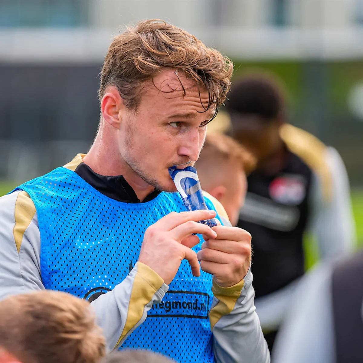 Soccer player in blue training vest using cola drink gel during outdoor team practice