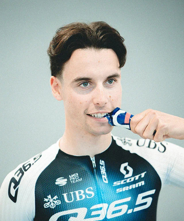 Cyclist in black and white Q36.5 team jersey eats raspberry drink gel