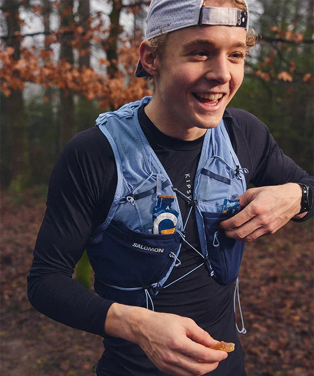 Trail runner eating orange fruit chew, wearing hydration vest in forest outdoors