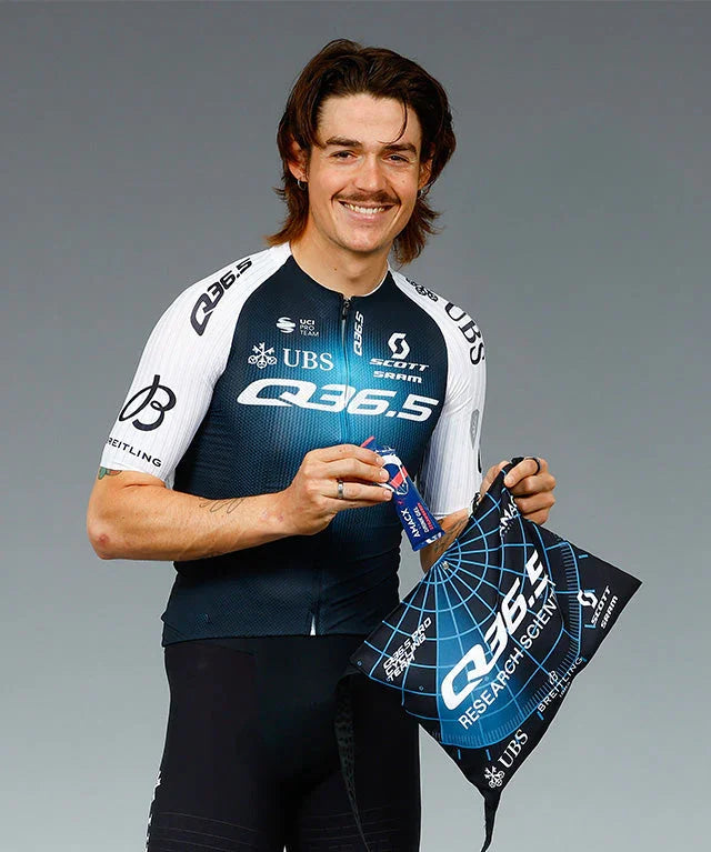 Smiling cyclist in Q36.5 team kit holding strawberry drink pouch and team musette bag