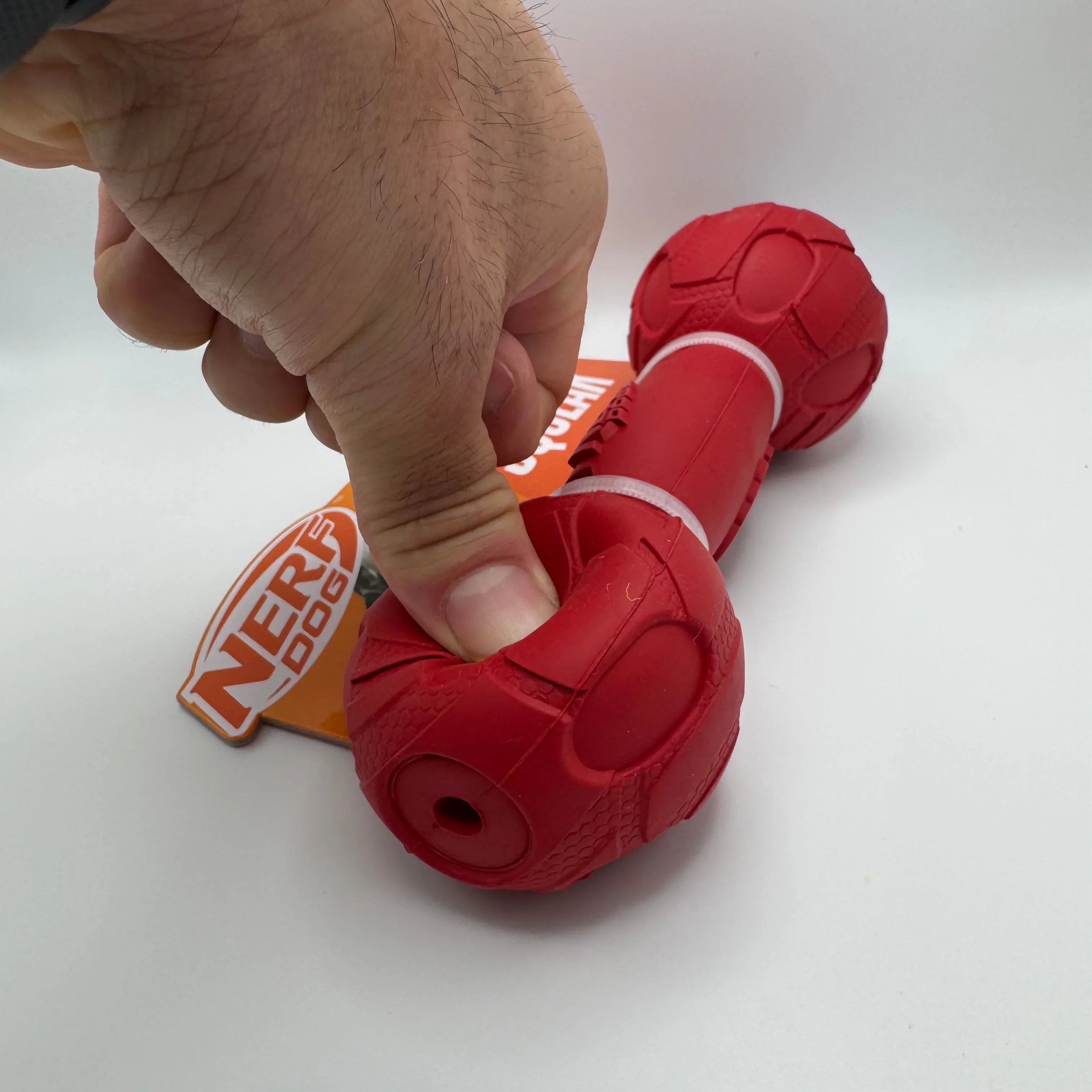 Hand squeezing red Nerf Dog rubber chew toy with packaging on white background