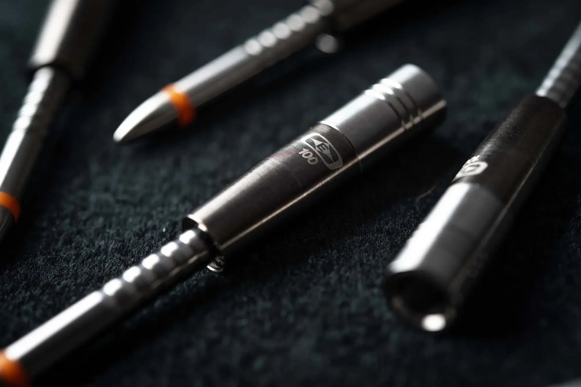Close-up of steel darts with engraved logo and orange rings on a dark textured surface