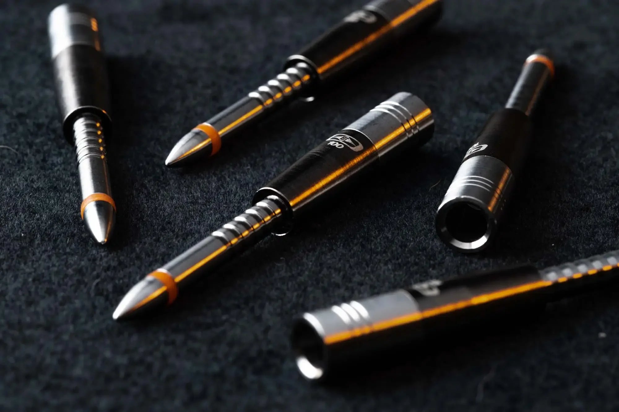 Close-up of black and silver dart barrels with orange rings on black fabric background