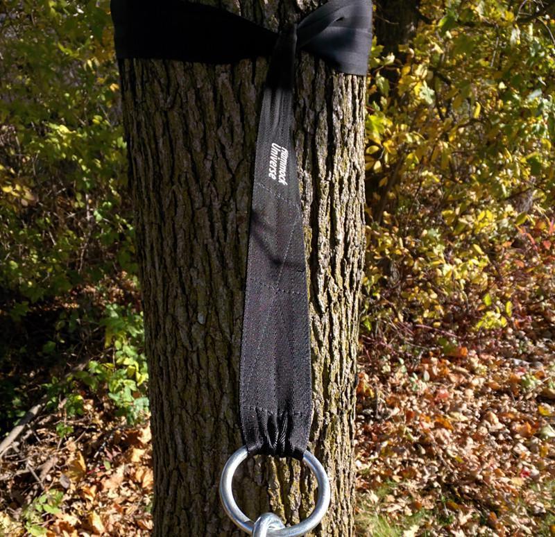 Black hammock tree strap with metal rings wrapped around a tree outdoors