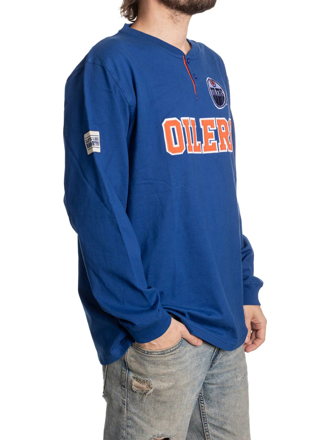 Man wearing blue Edmonton Oilers long sleeve Henley shirt with logo and jeans