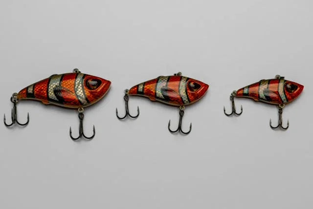 Three red and black fish-shaped fishing lures with treble hooks on a grey background.