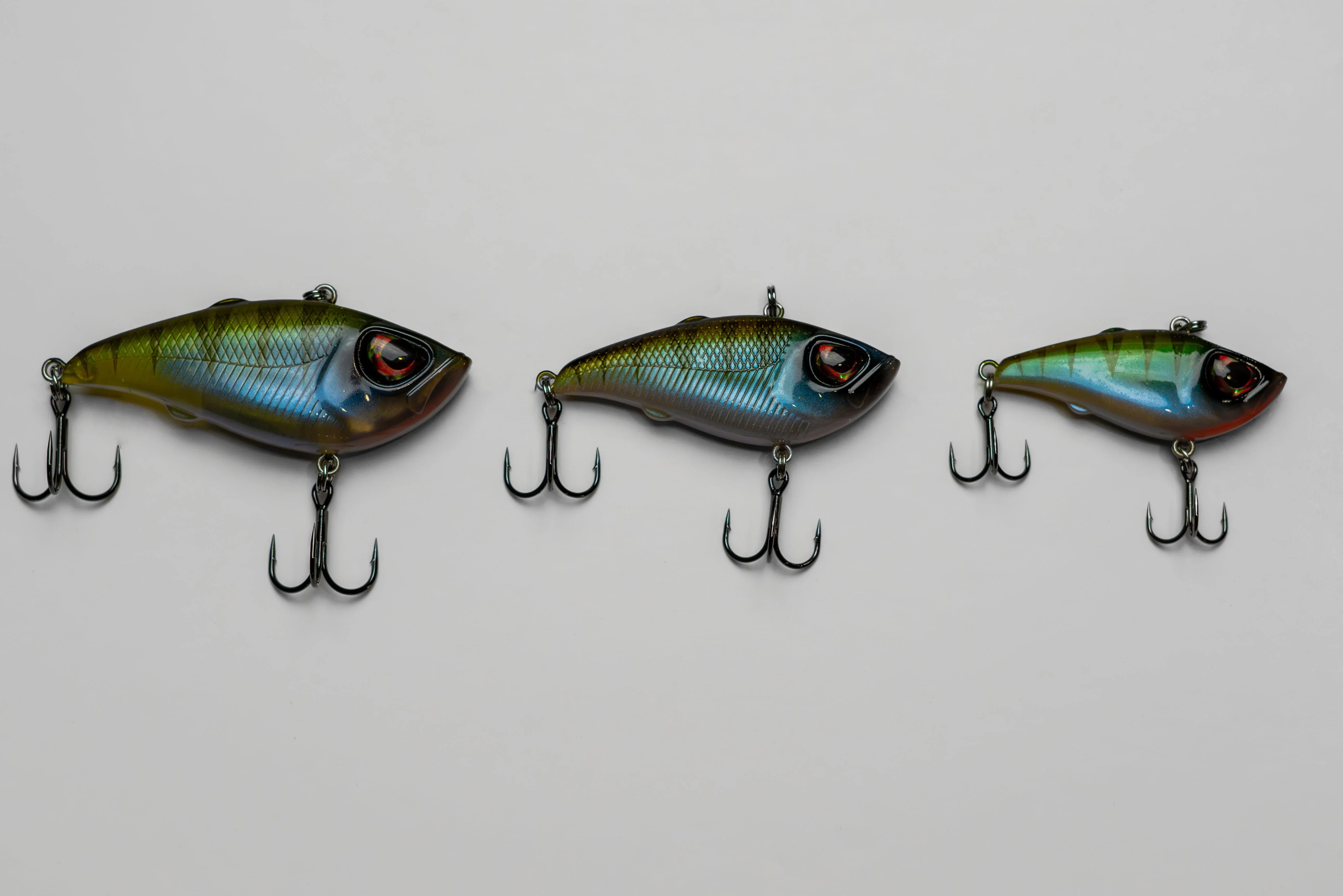 Three colorful fish-shaped fishing lures with treble hooks on a white background