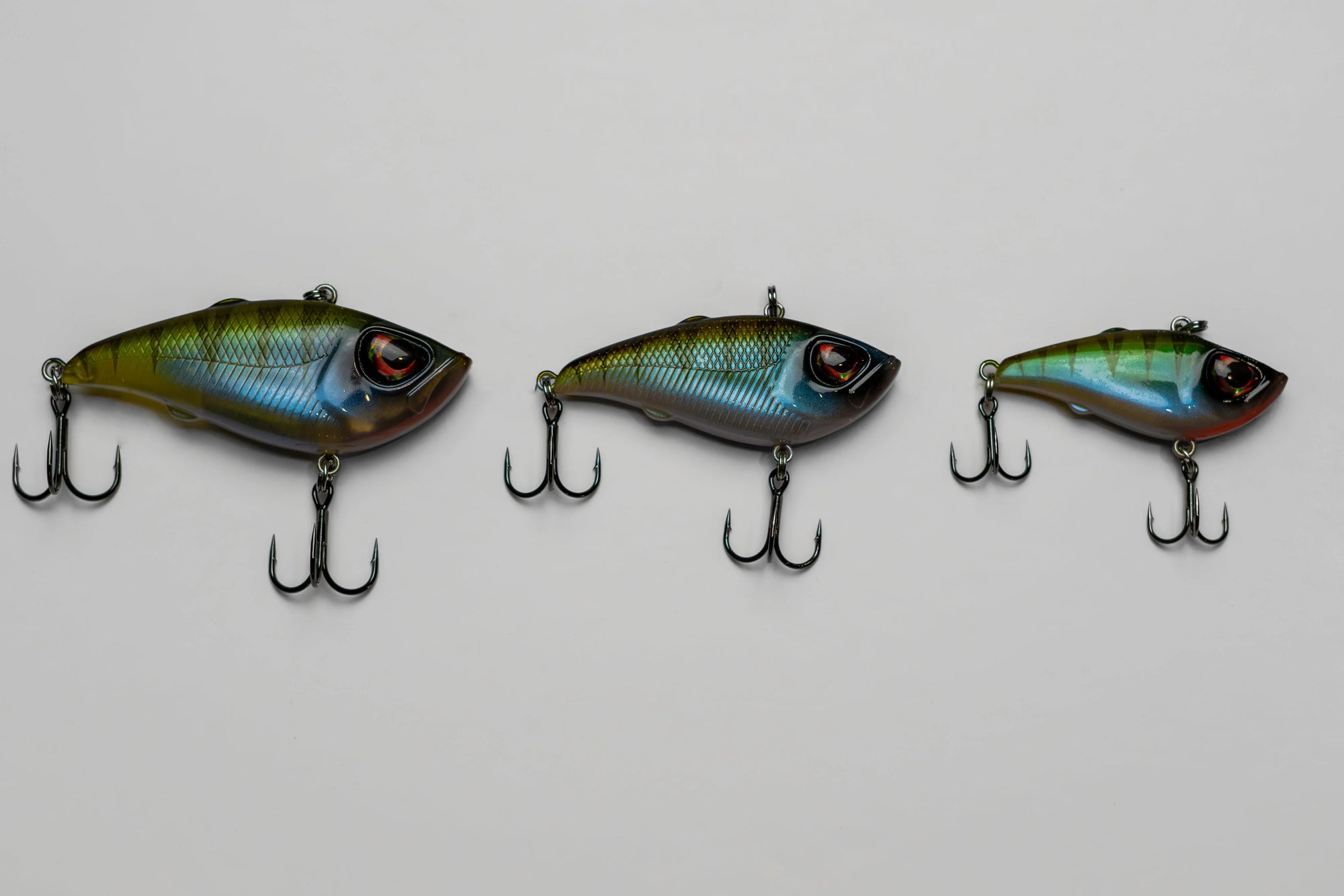 Three colorful fish-shaped fishing lures with treble hooks on a white background