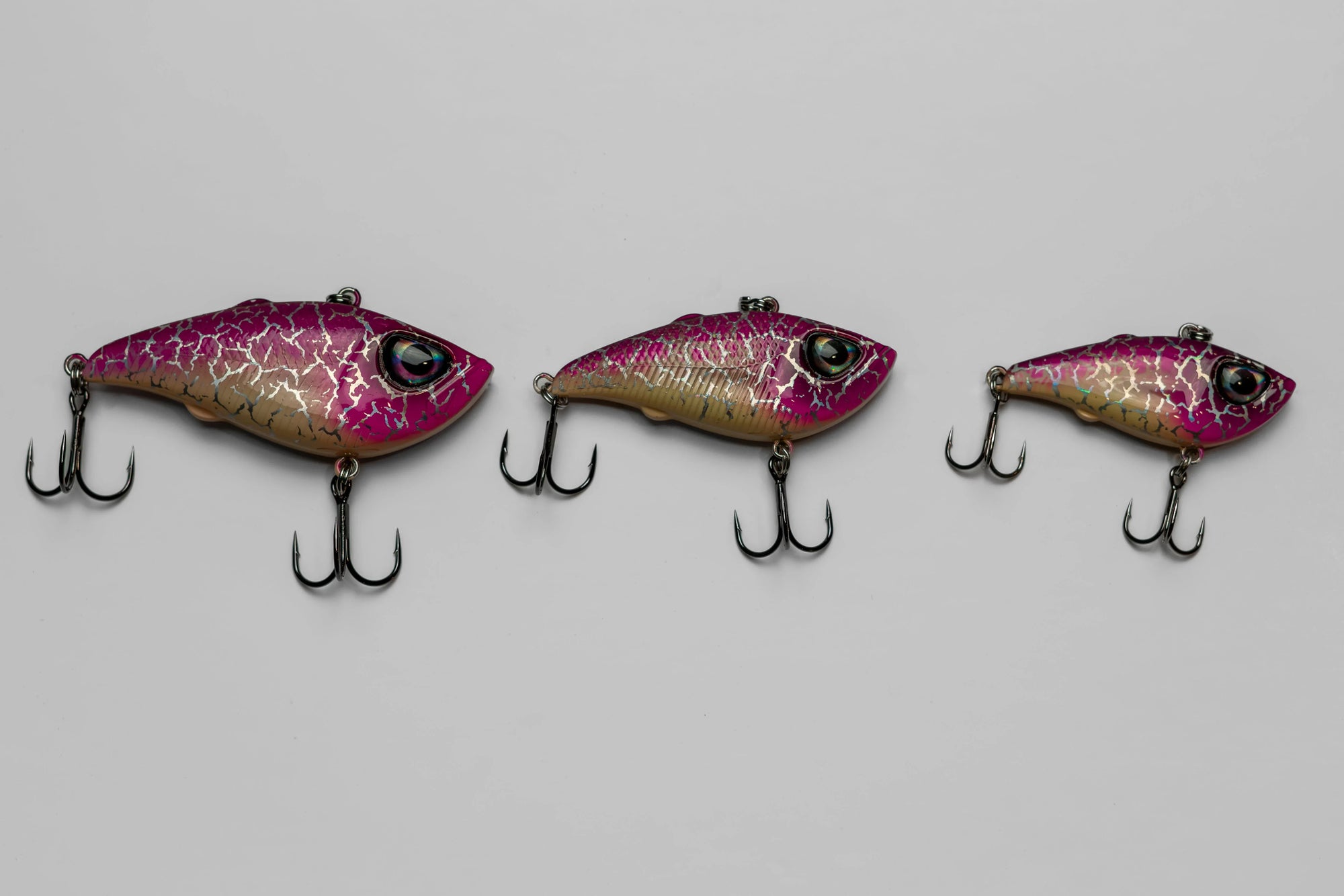Three pink and gold fishing lures with treble hooks on a light gray background