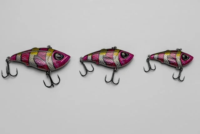 Three pink and yellow striped fish-shaped fishing lures with treble hooks on gray background