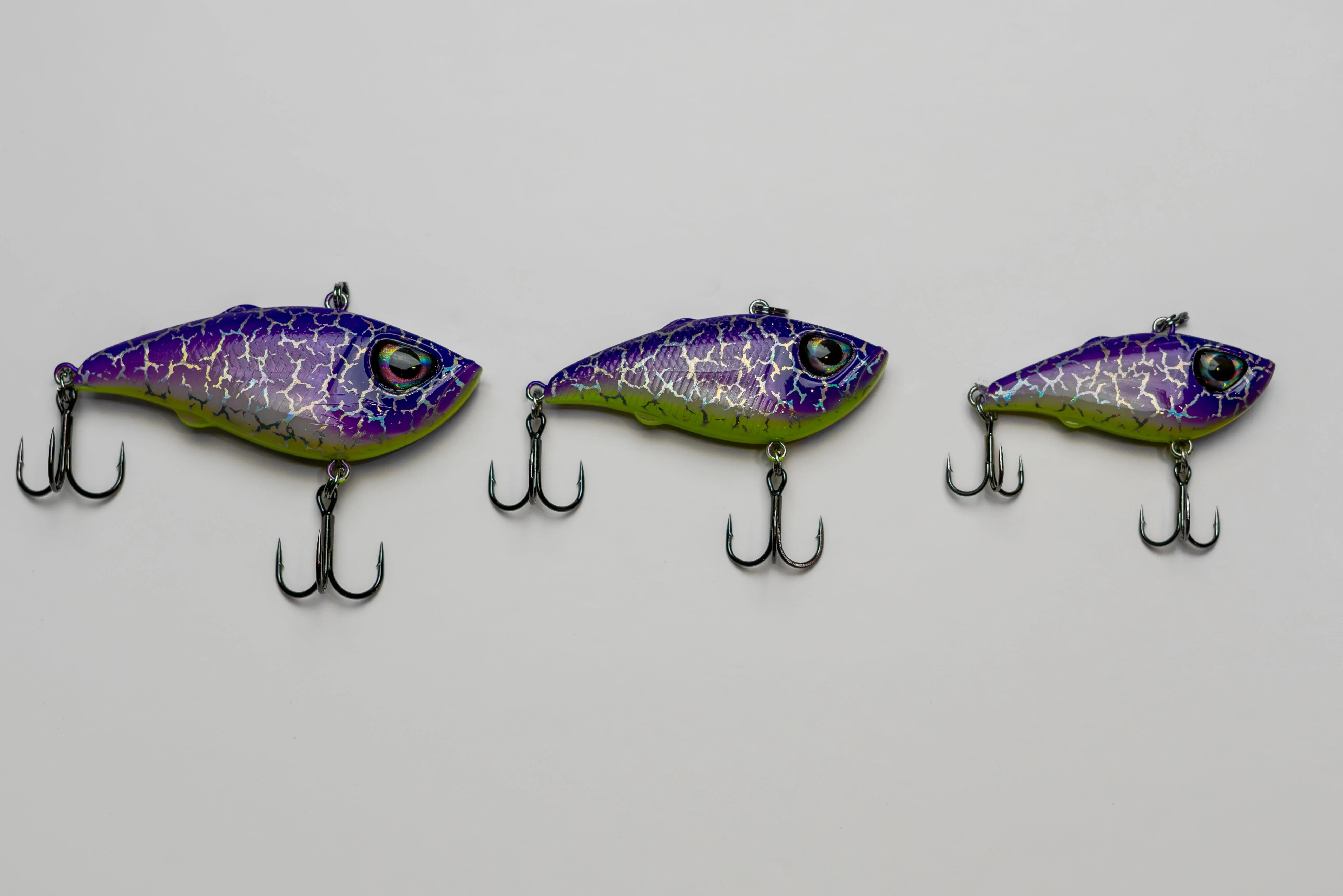 Three purple and green crackle finish fishing lures with treble hooks on white background