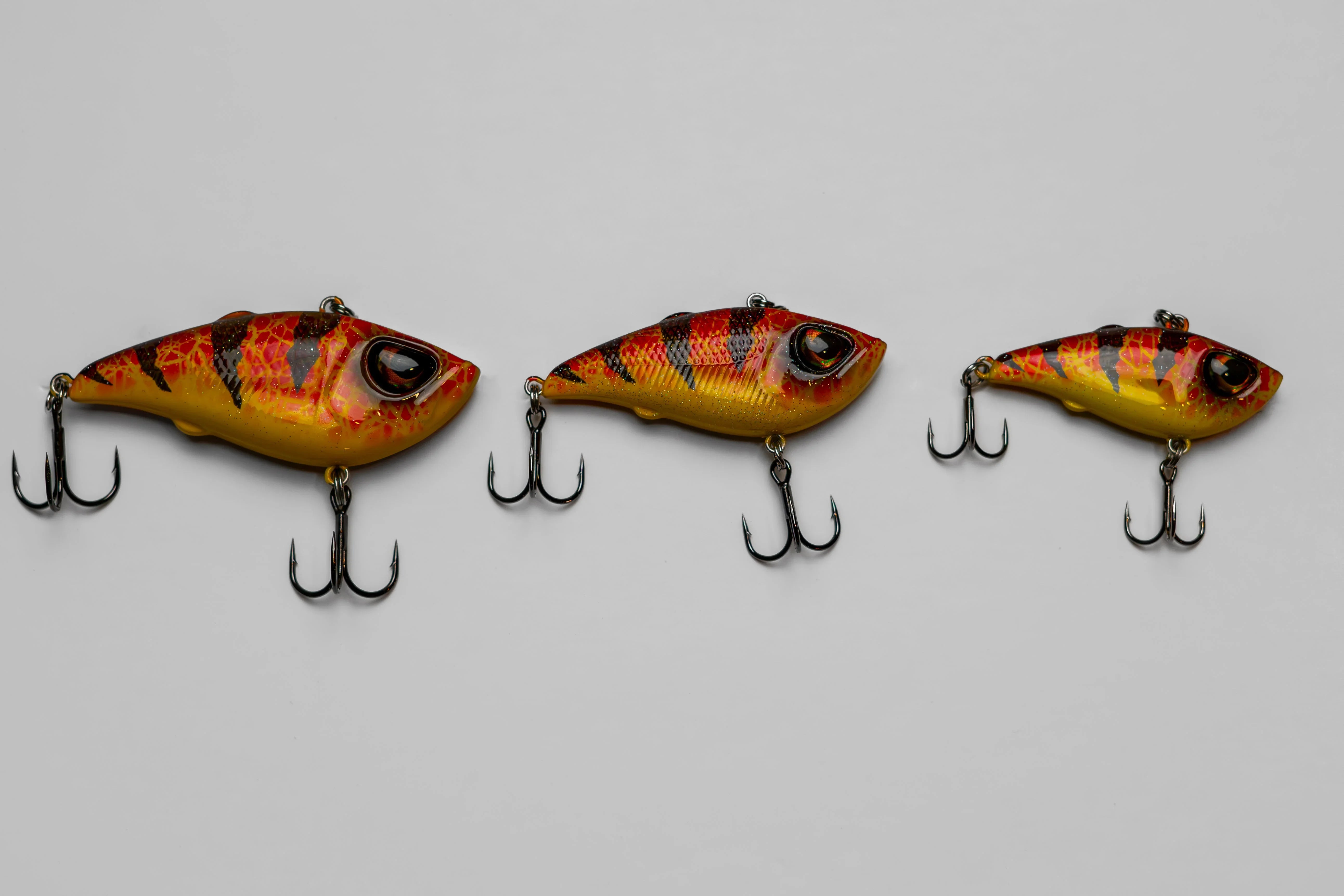 Three yellow and red fish-shaped fishing lures with treble hooks on a gray background.