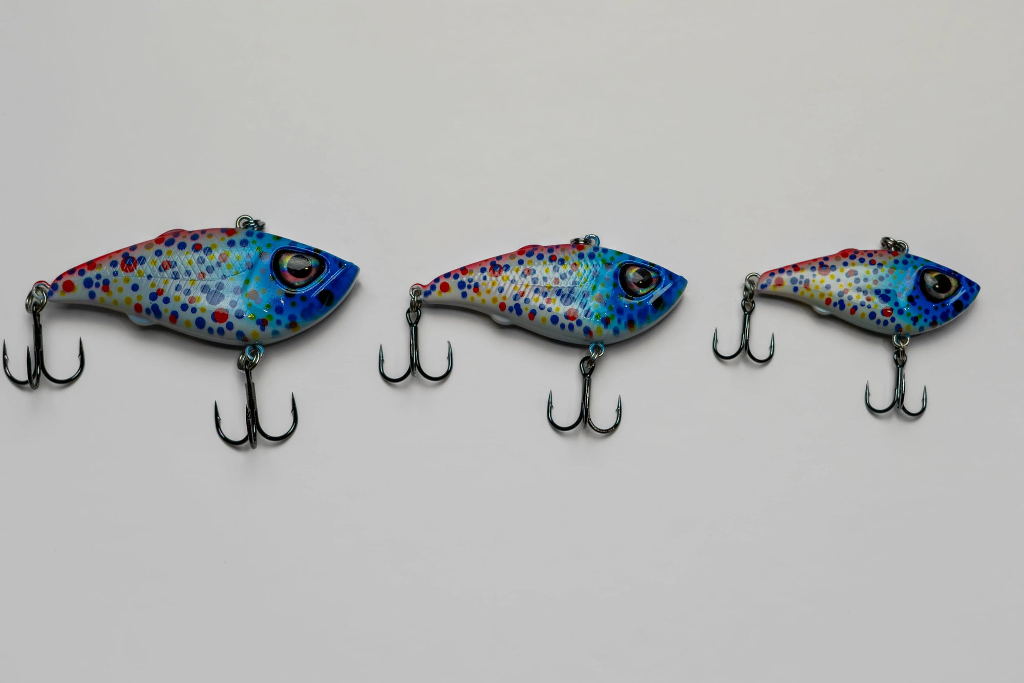 Three colorful fish-shaped fishing lures with treble hooks on white background