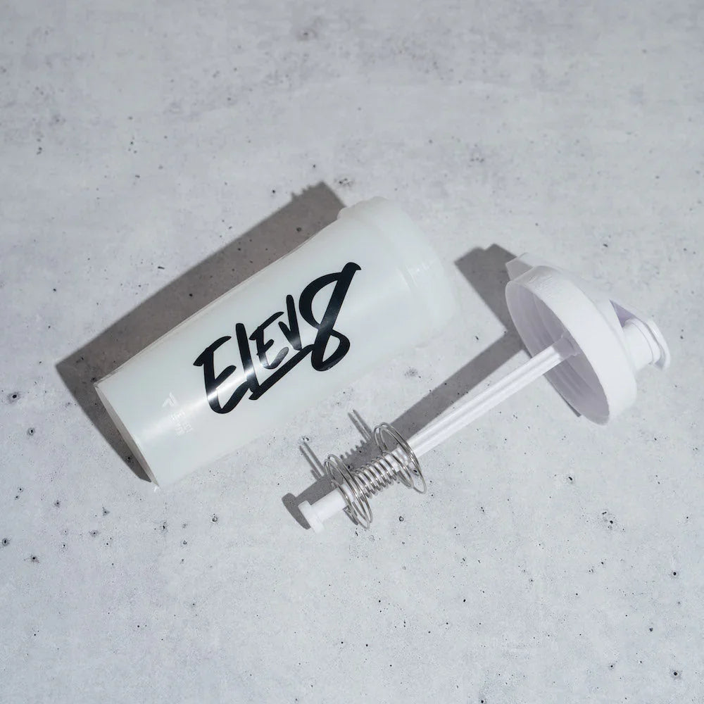 White ELEV8 protein shaker bottle and lid with spring mixer on concrete surface