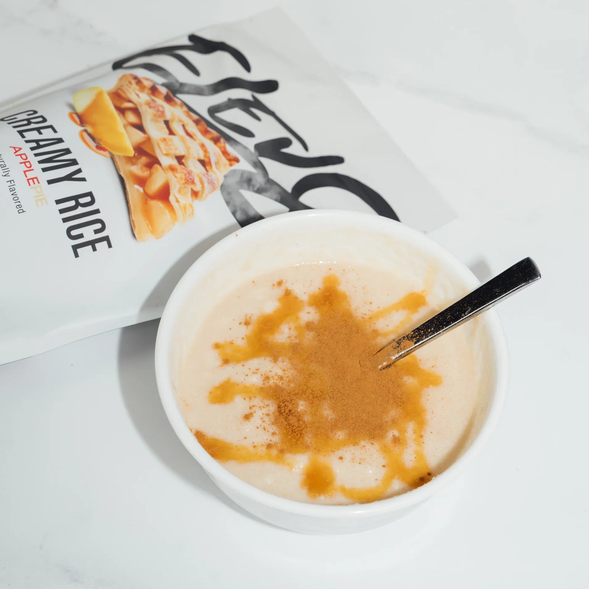 Bowl of creamy rice pudding with cinnamon, spoon, and apple pie flavored packaging