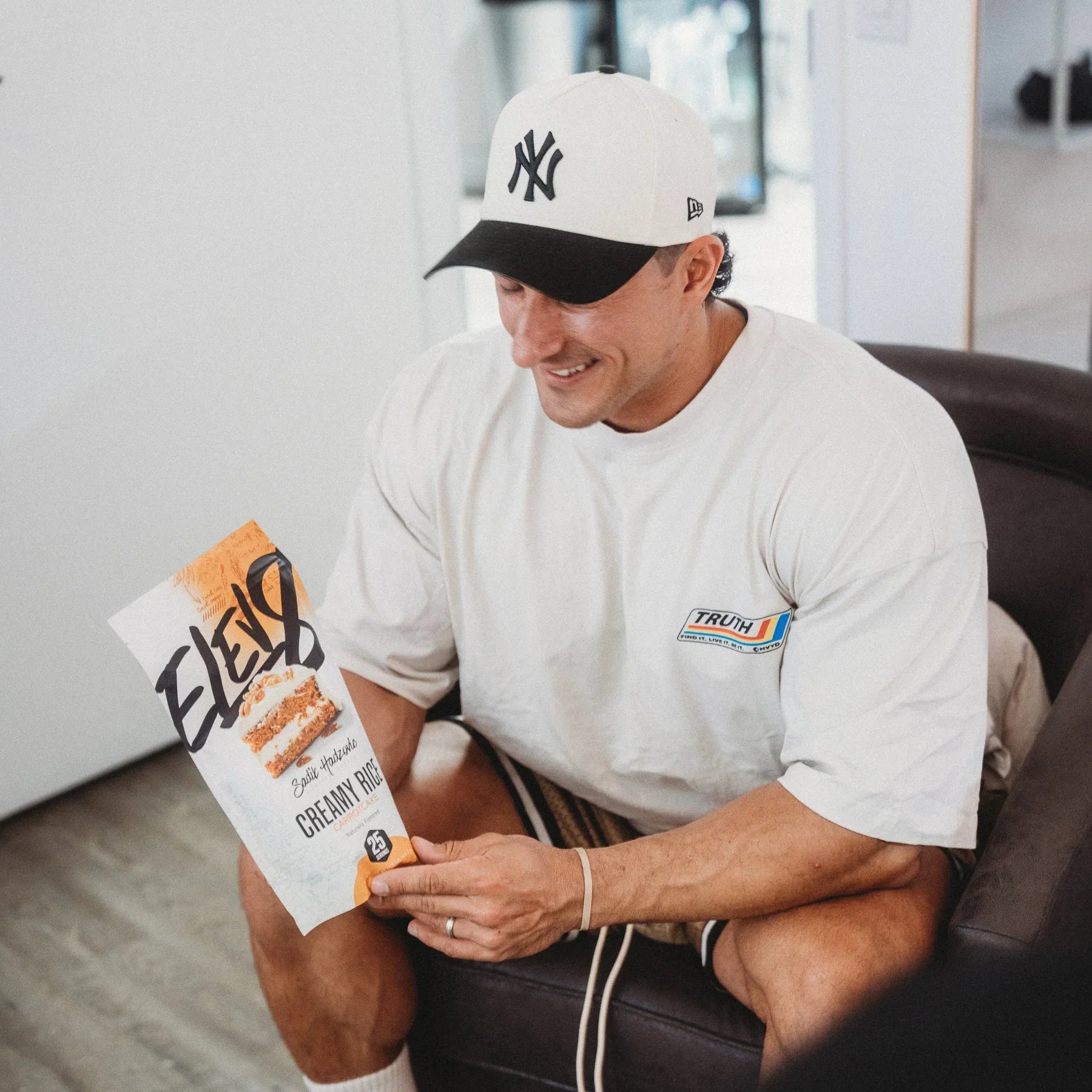 Man in NY Yankees hat holding ELEAT Creamy Rice cereal in modern living room