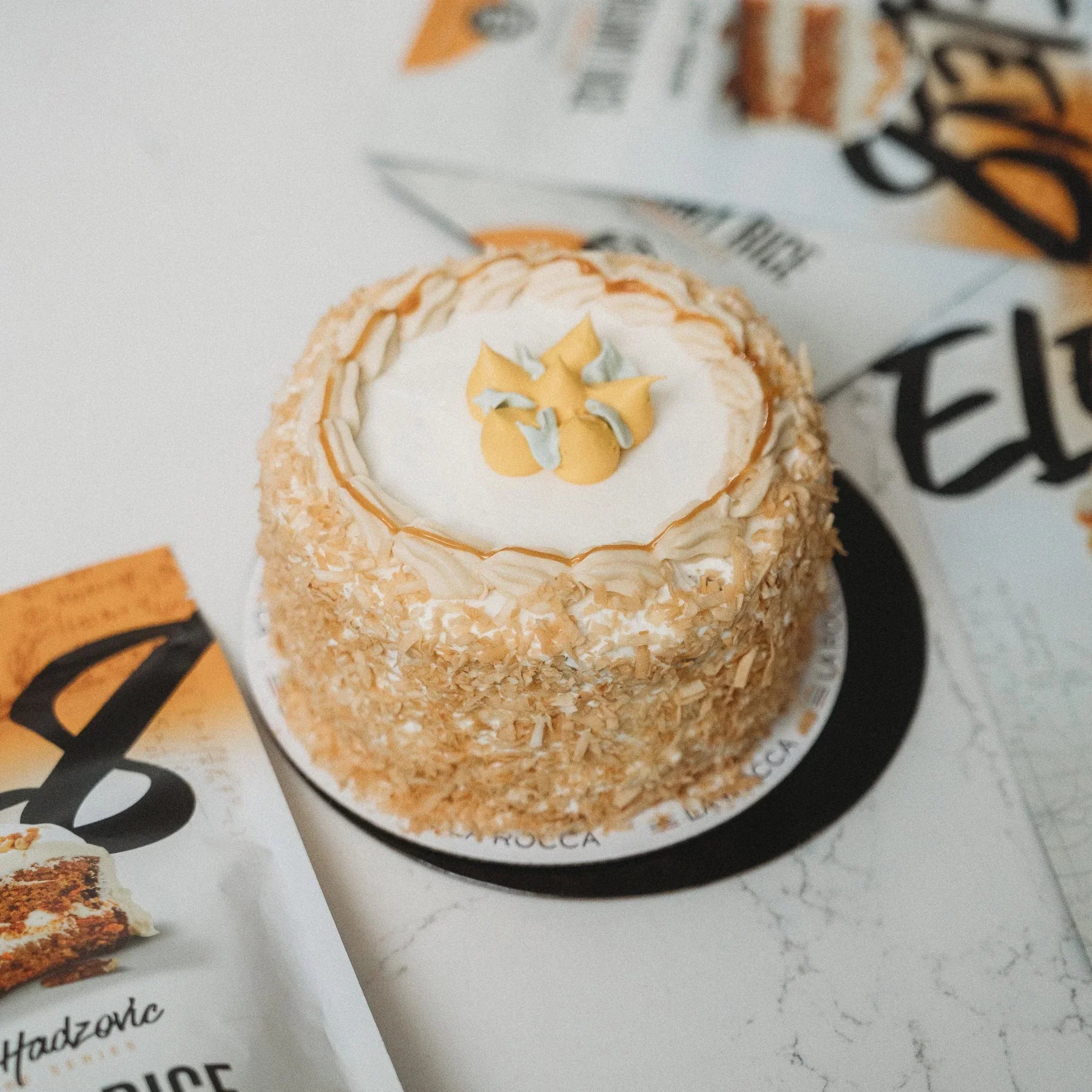 Coconut layered cake with cream frosting on a marble surface, surrounded by branded packaging
