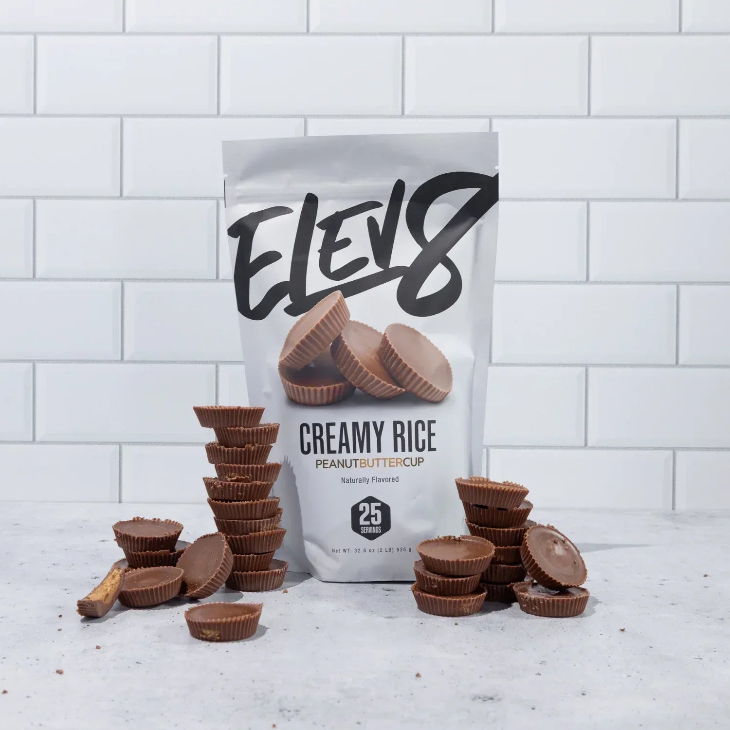 Elev8 Creamy Rice Peanut Butter Cup candy stacked in front of branded bag on white tile background