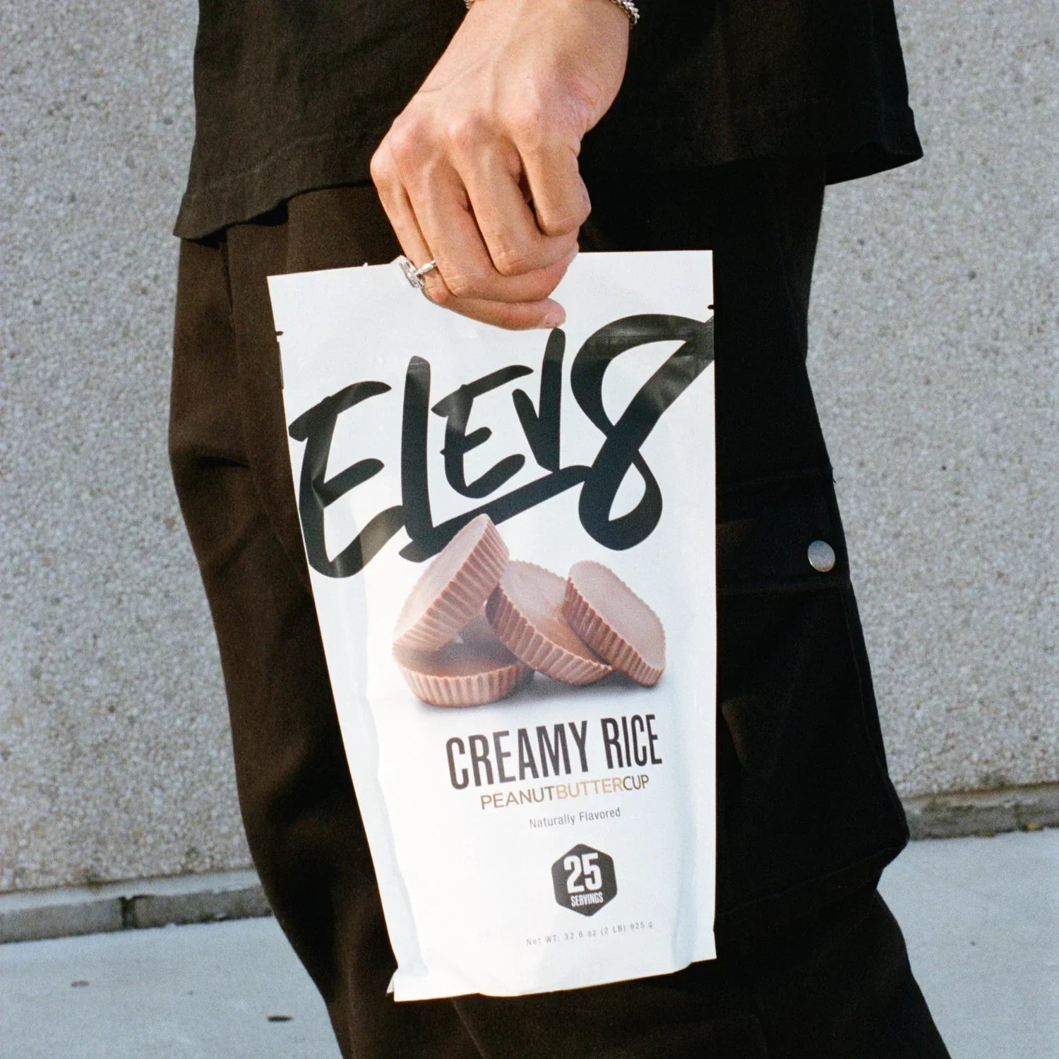 Person holding Elev8 Creamy Rice Peanut Butter Cup protein powder bag outdoors
