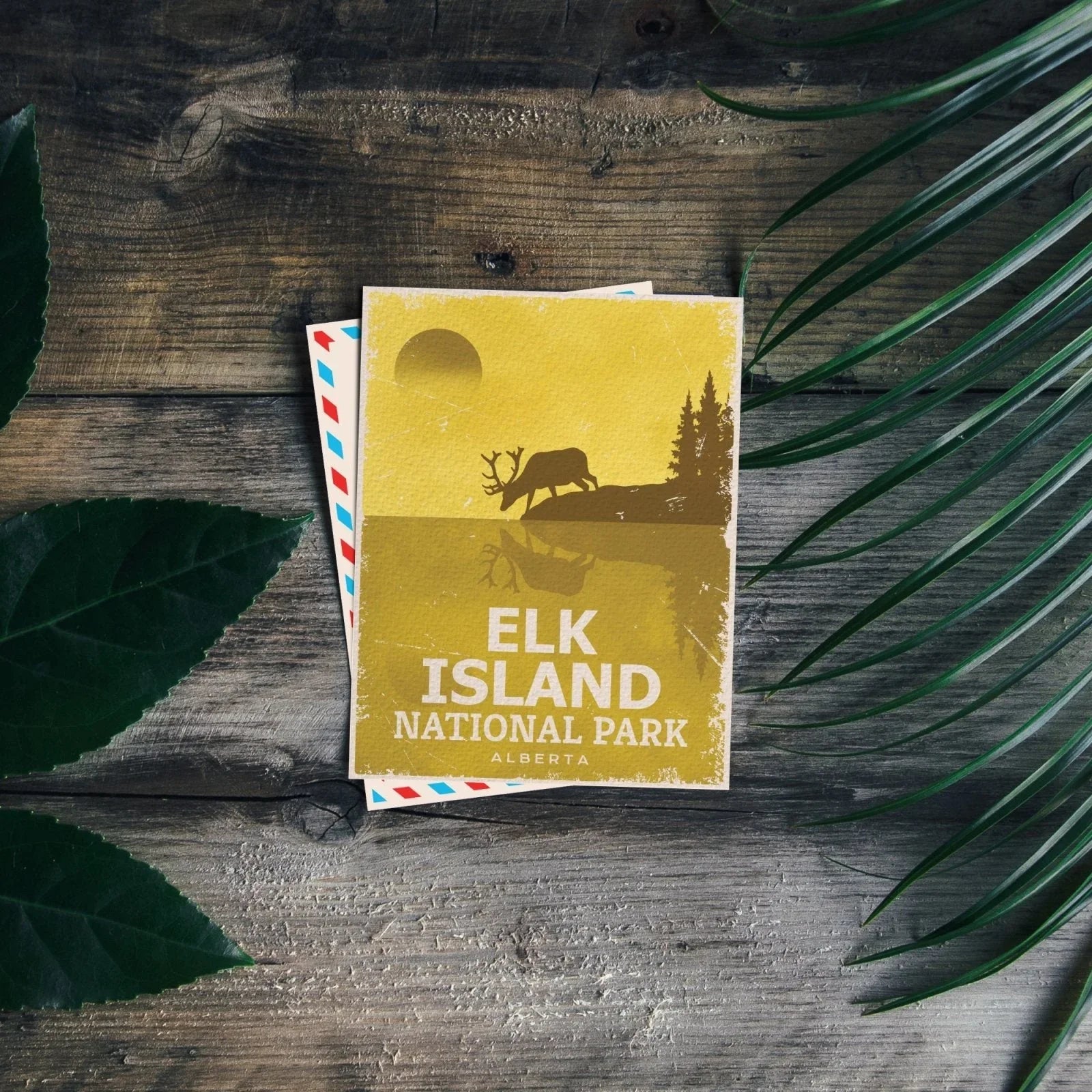 Elk Island National Park postcard on wood, with green leaves and silhouette elk design.