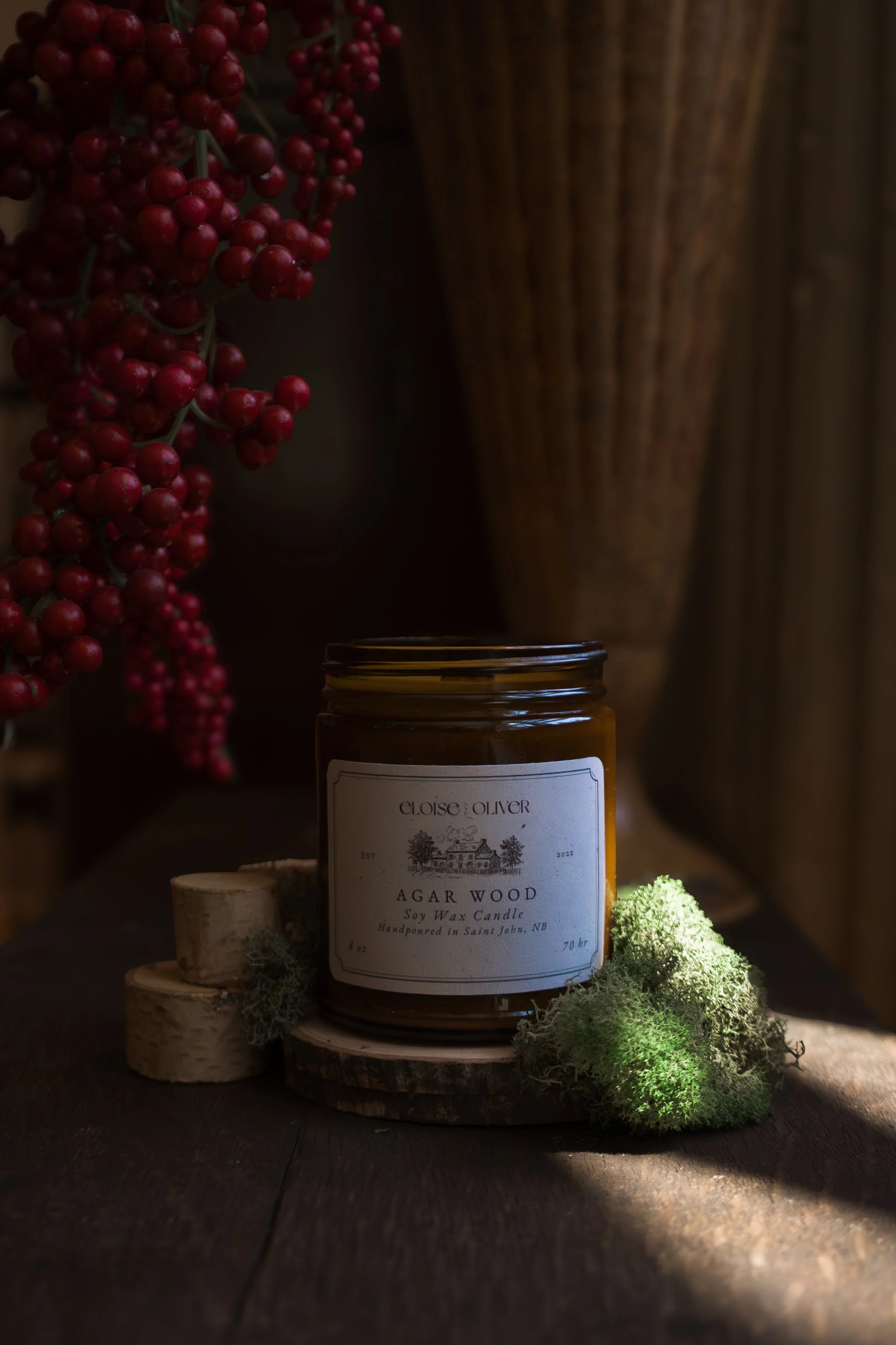 Agar wood soy wax candle on wood slice with moss, red berries, and rustic decor