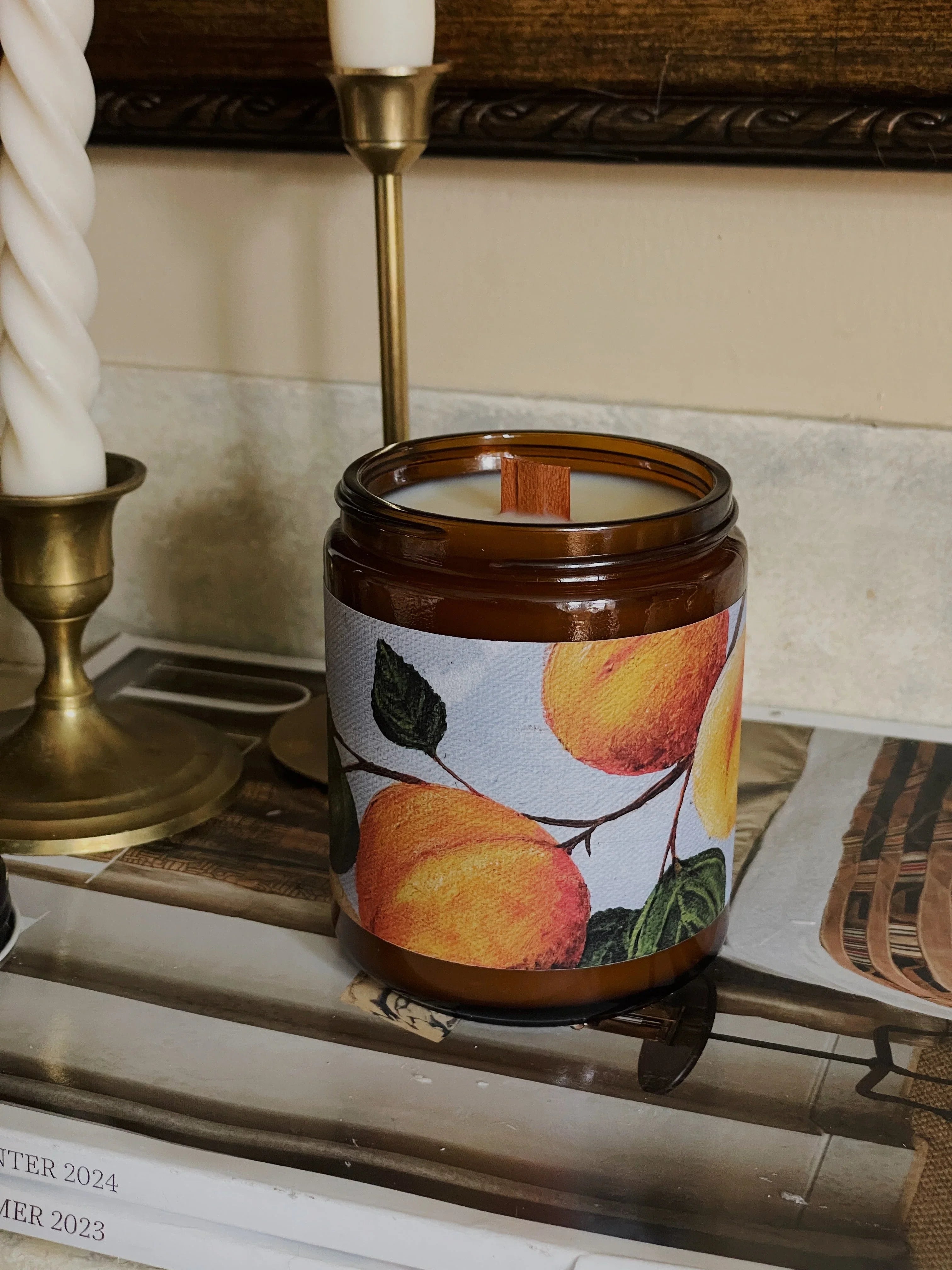 Scented soy candle in amber jar with peach illustration on cozy home decor table