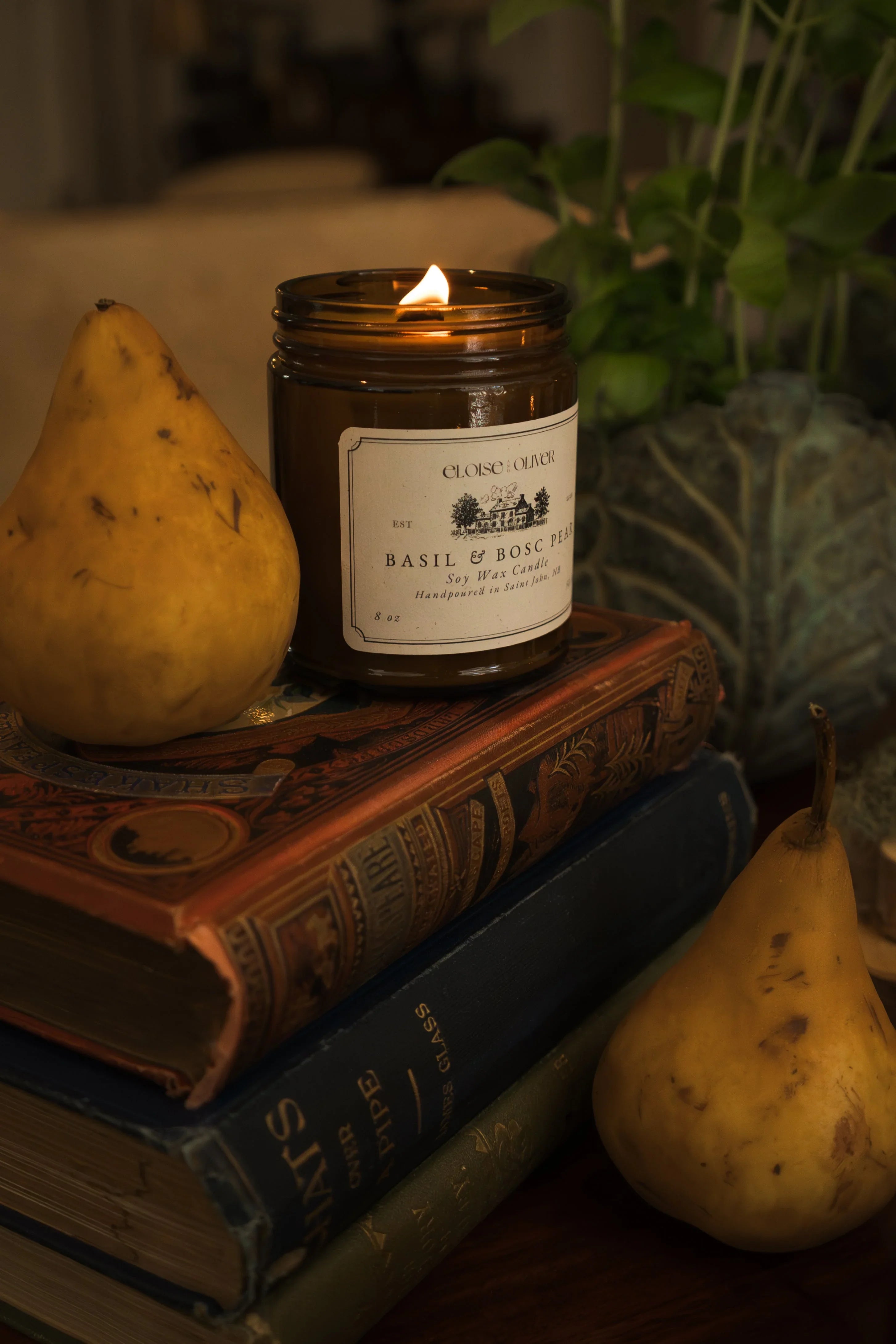 Basil & Bosc Pear soy wax candle lit beside pears and vintage books, cozy home decor scene