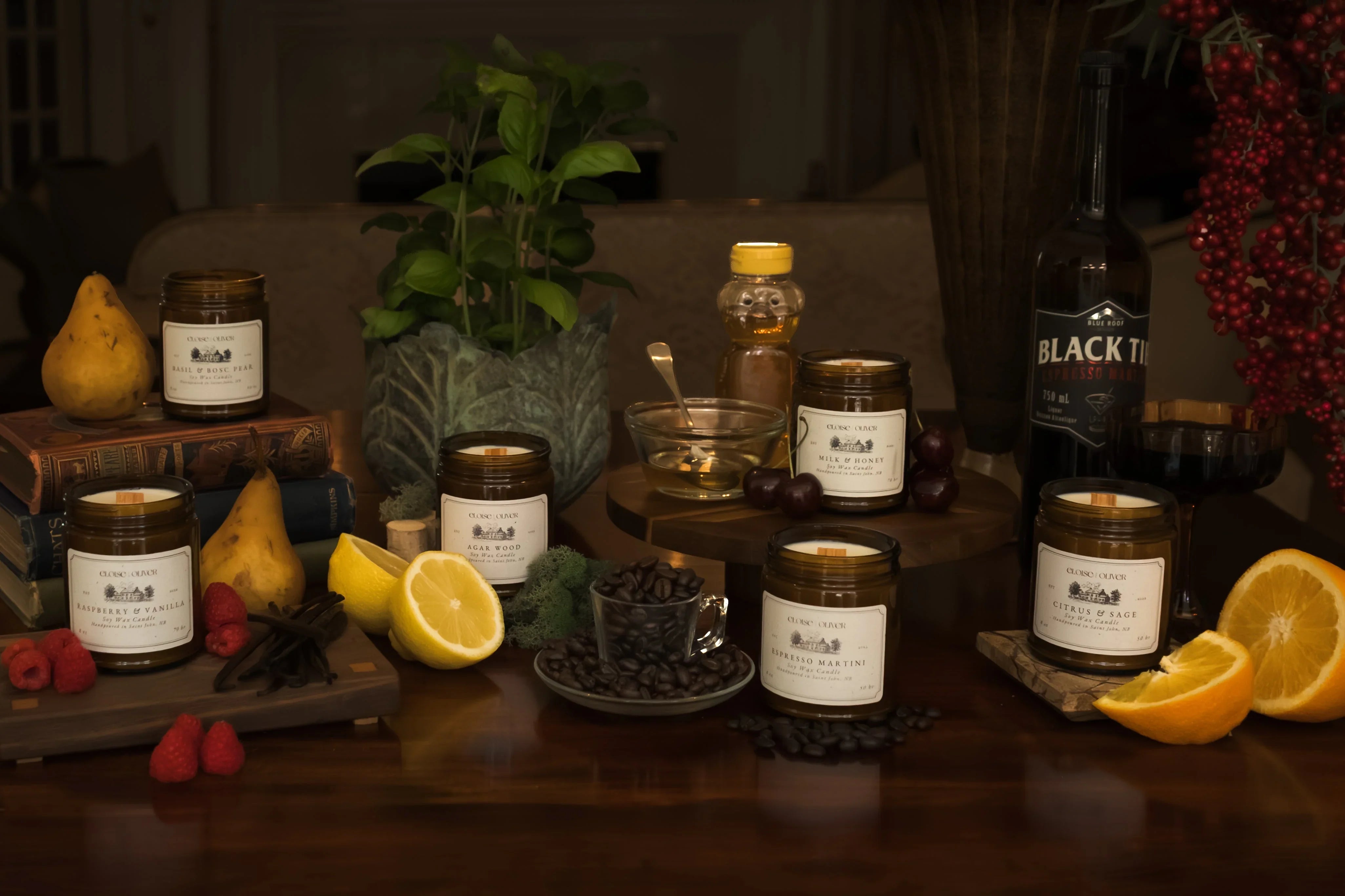 Assorted scented candles with fruits, honey, coffee beans, and books on a wooden table