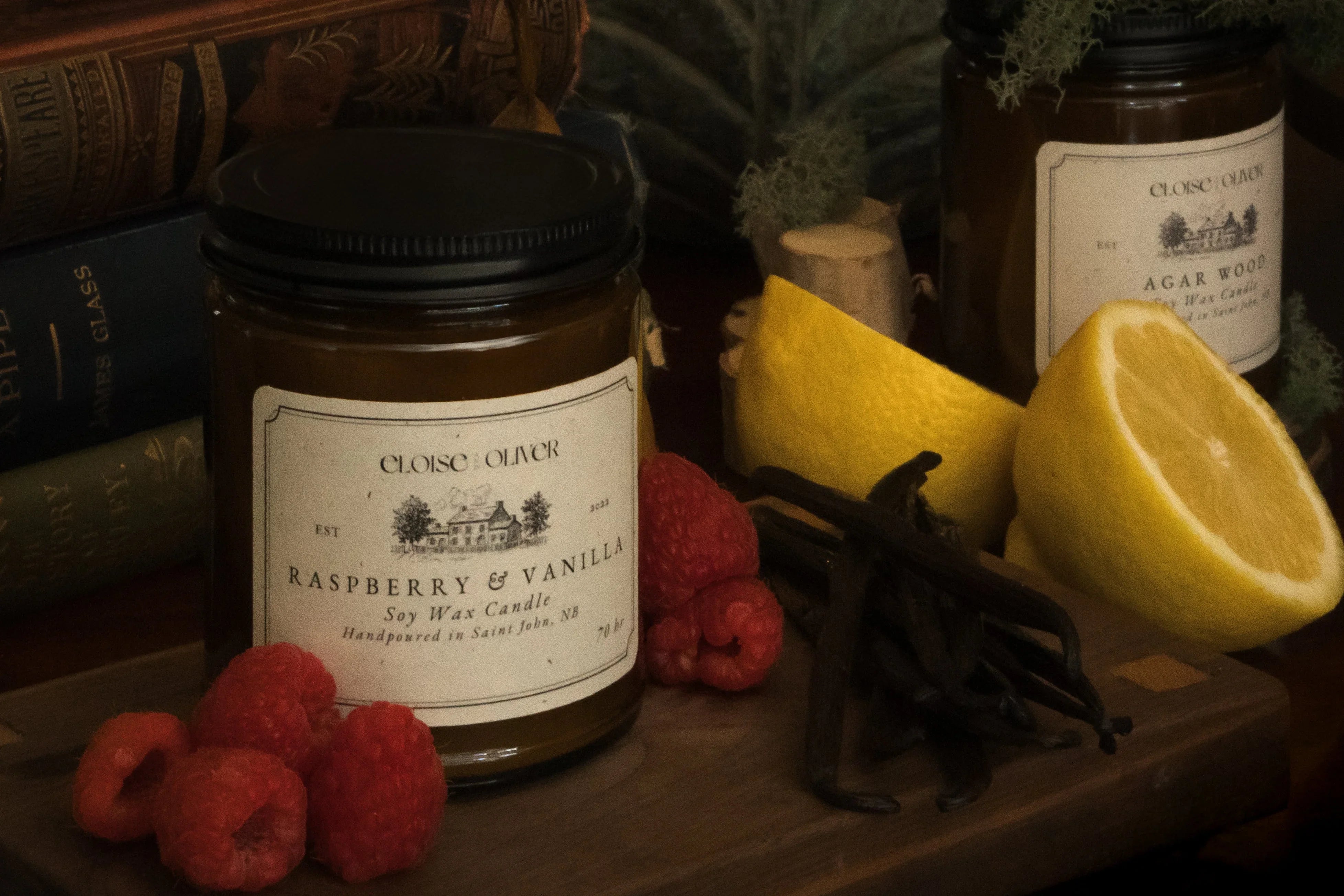 Raspberry and vanilla soy wax candle with raspberries, vanilla beans, and lemon on wooden board
