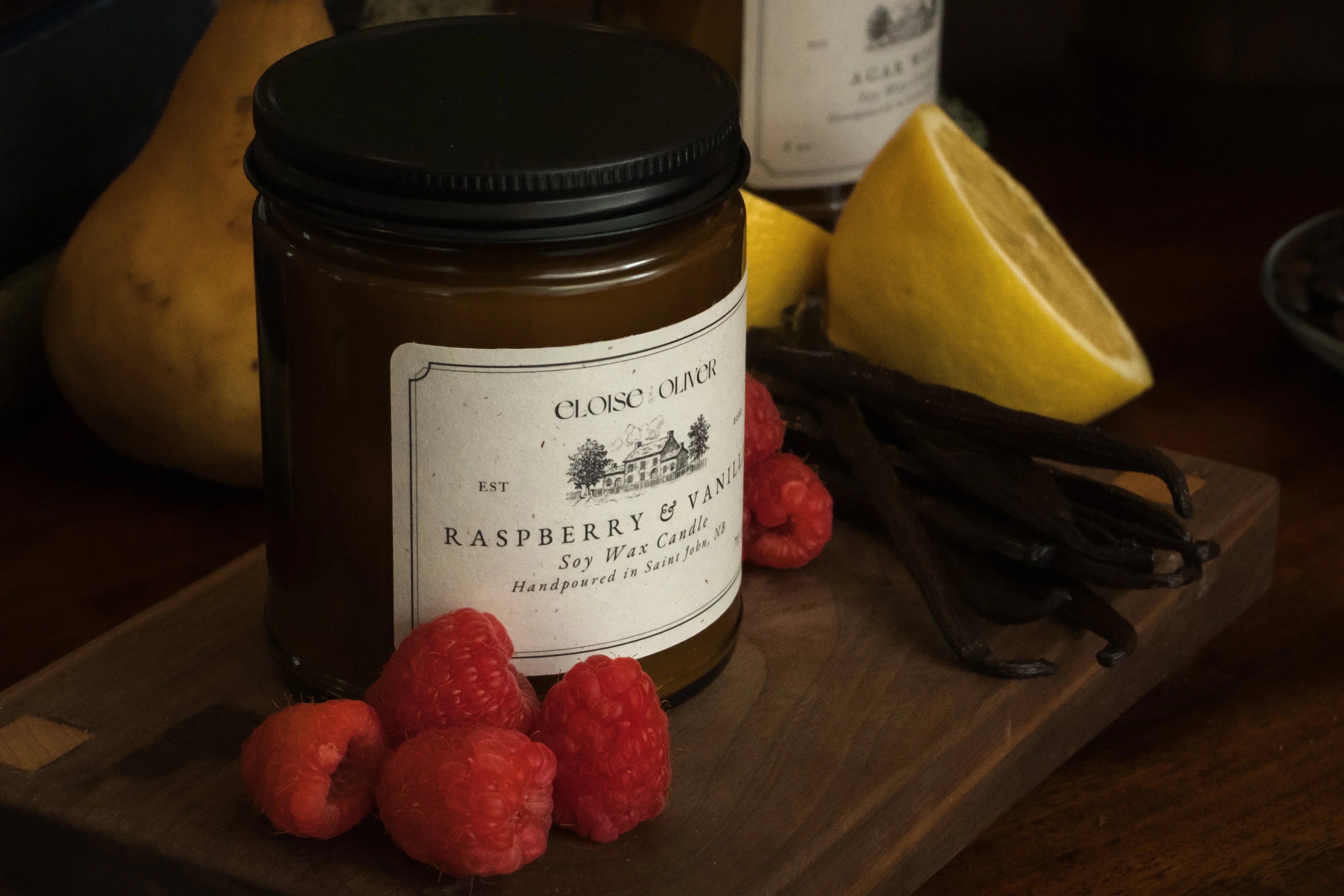 Raspberry and vanilla soy wax candle with fresh raspberries, vanilla beans, and lemon on wood