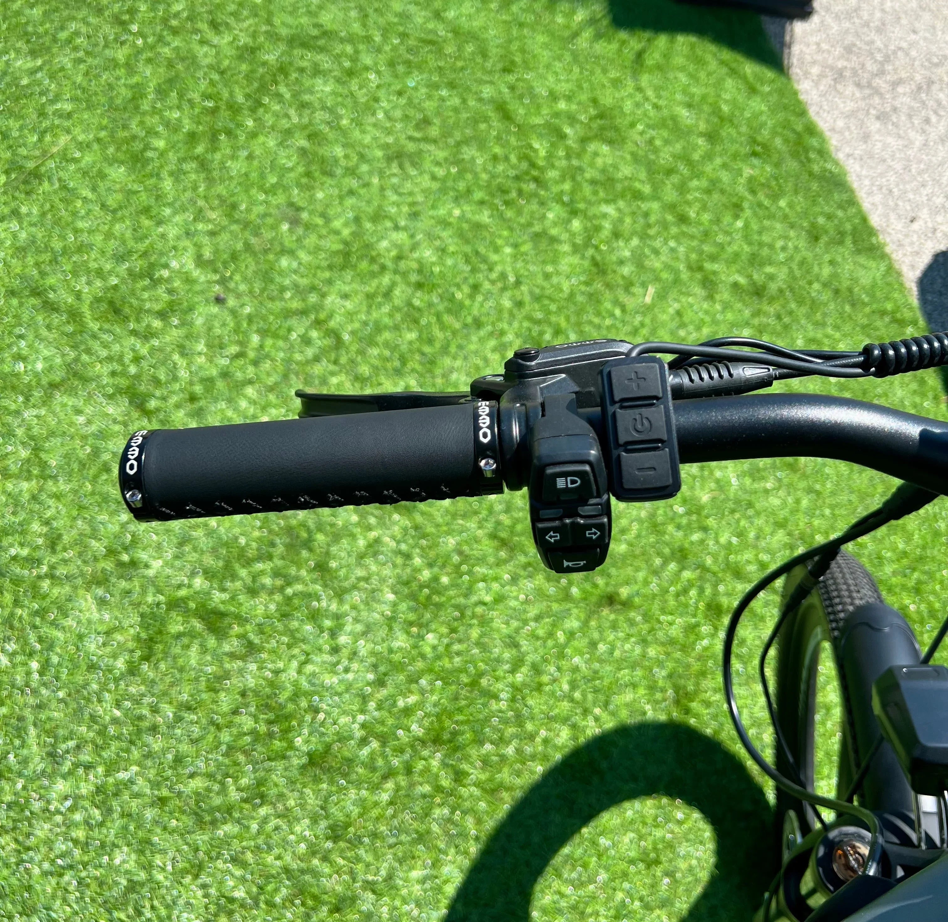 Electric bike handlebar with control buttons and OUNO grip on artificial grass