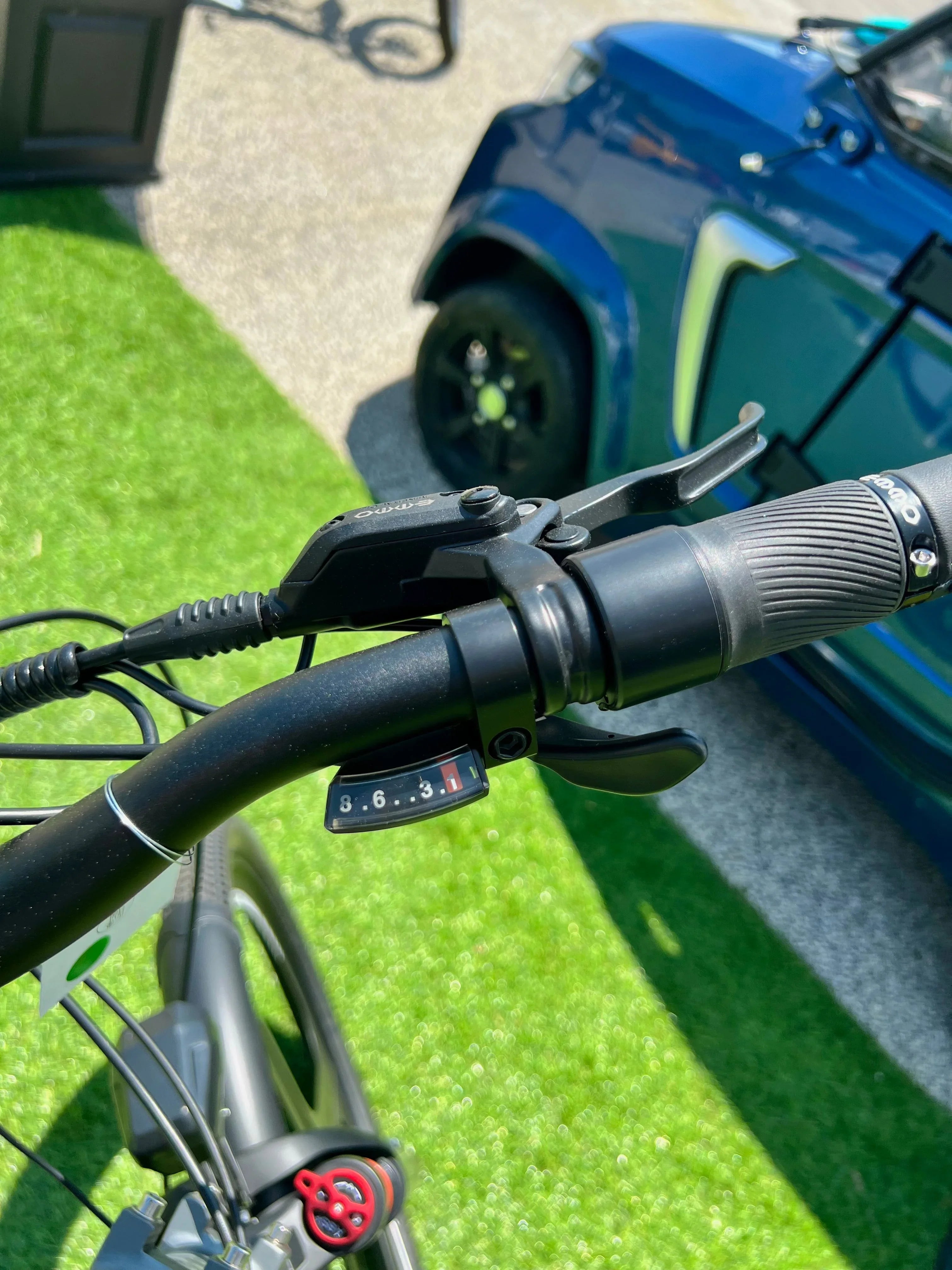 Bicycle handlebar with Shimano gear shifter, green artificial turf, blue car in background
