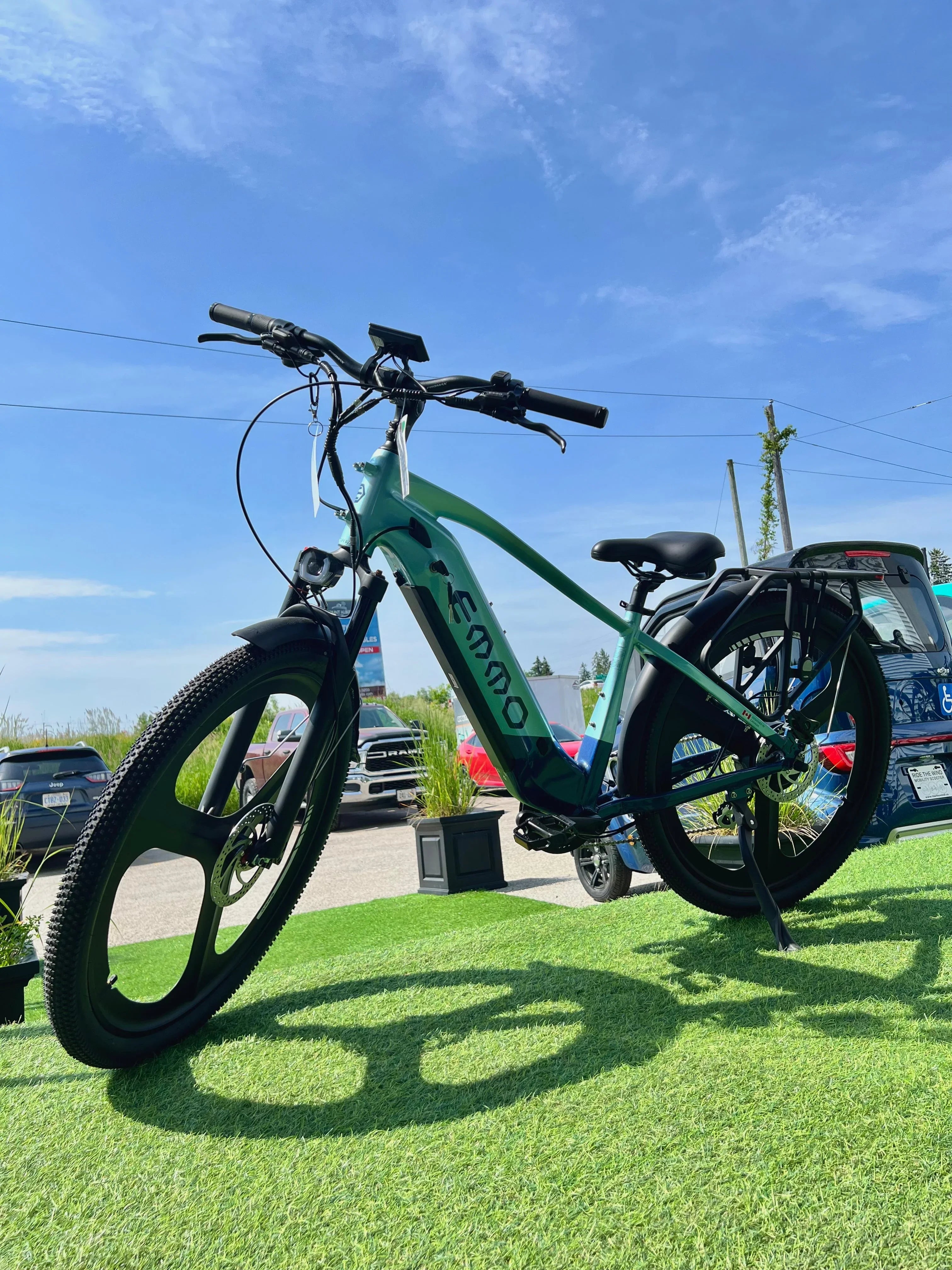 Electric fat tire bike on display outdoors, green grass, blue sky, parked cars background