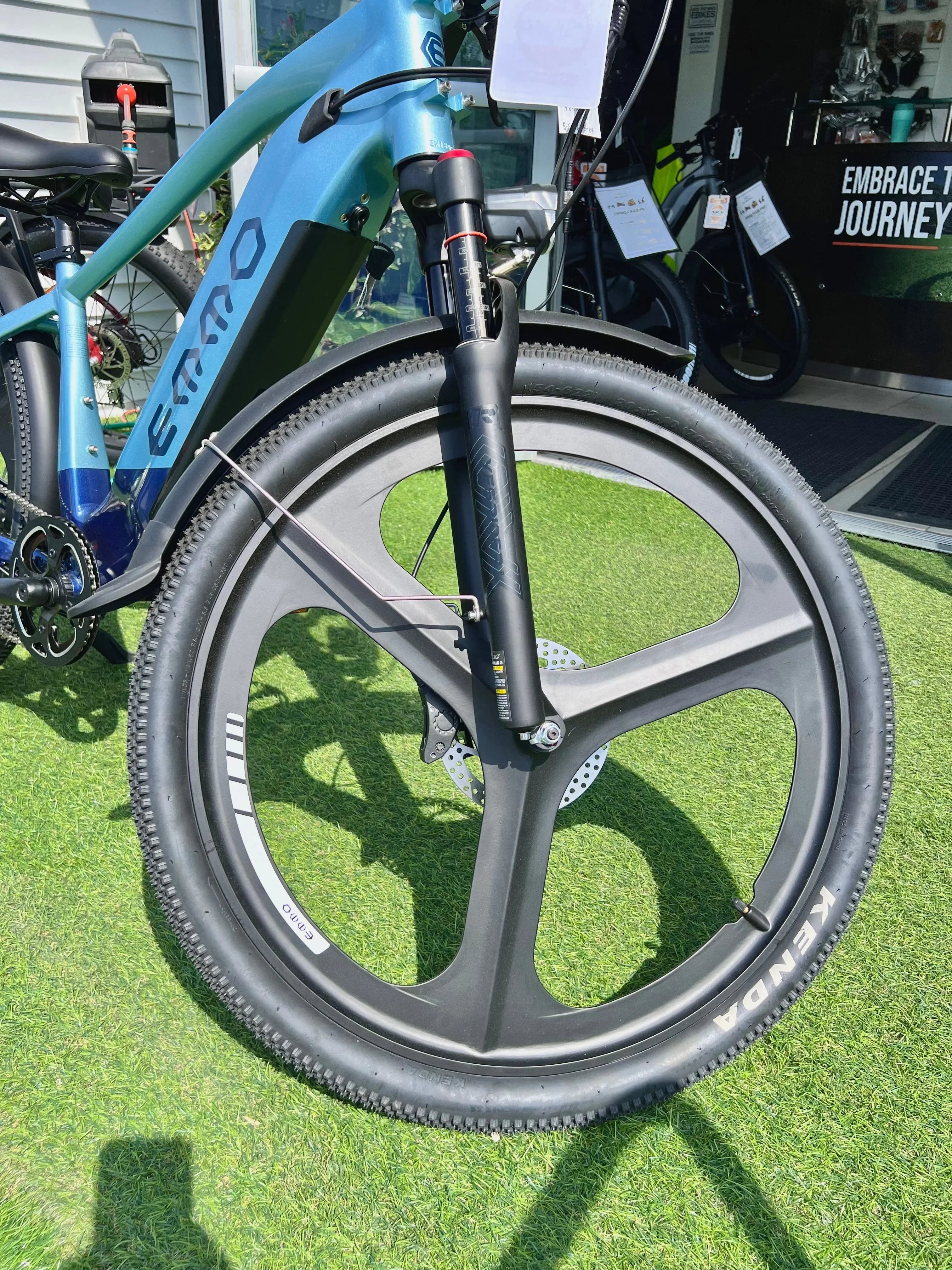 Blue EMMO electric bike with black mag wheels and Kenda tires on green grass outside store