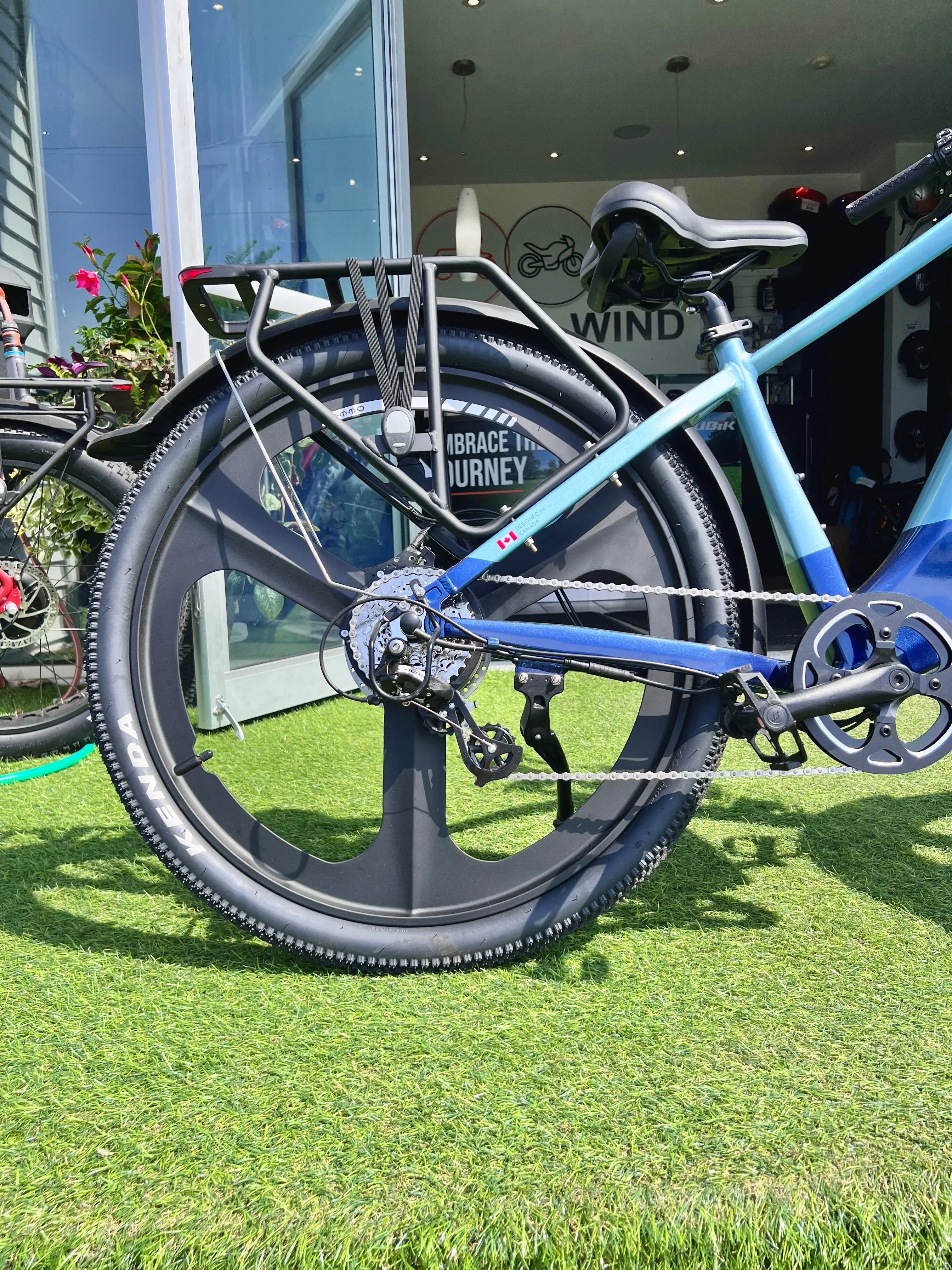 Close-up of blue bicycle with solid rear wheel and gear set outside bike shop on grass
