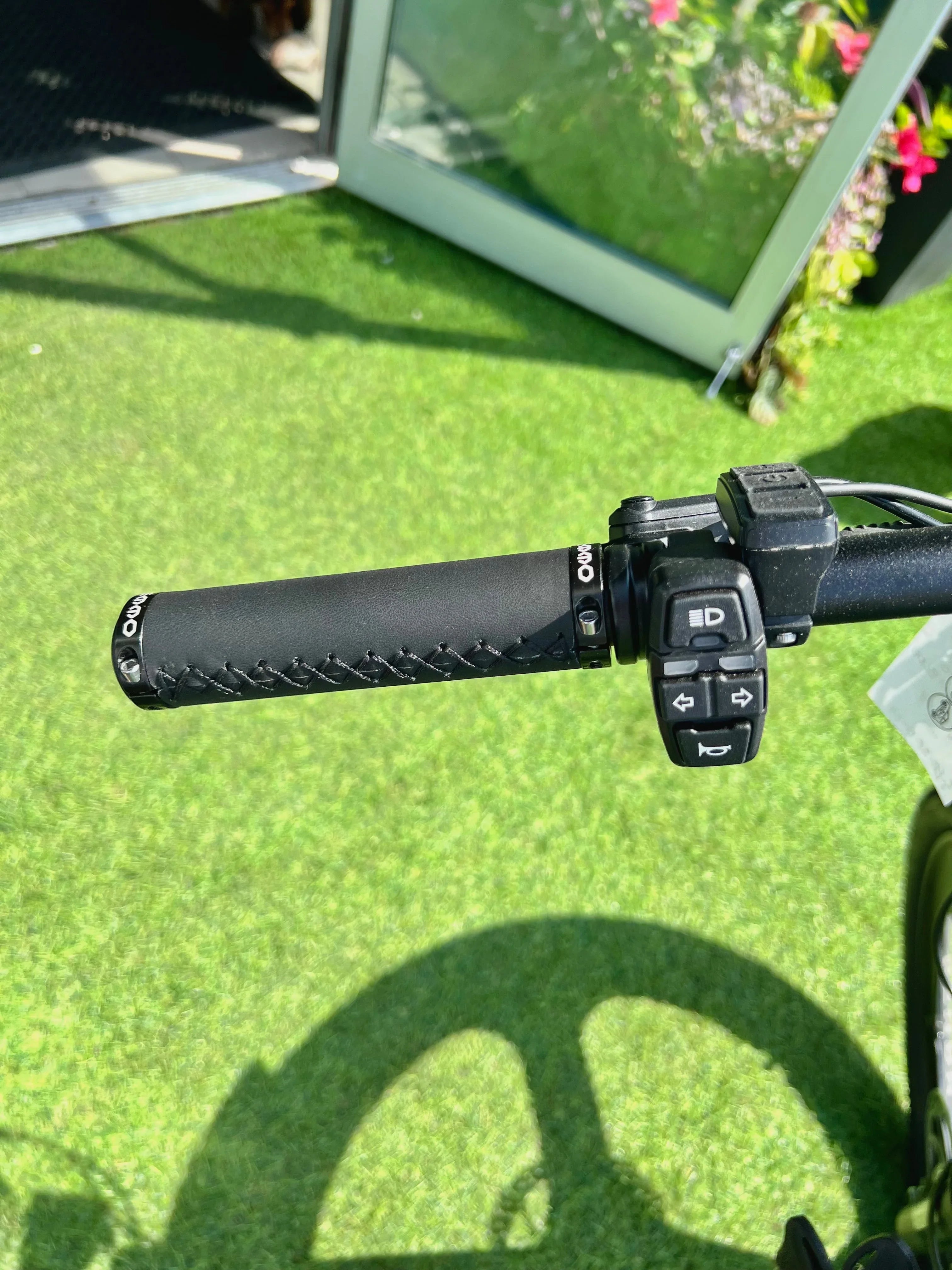 Black e-bike handlebar grip with control switches, outdoor grass background