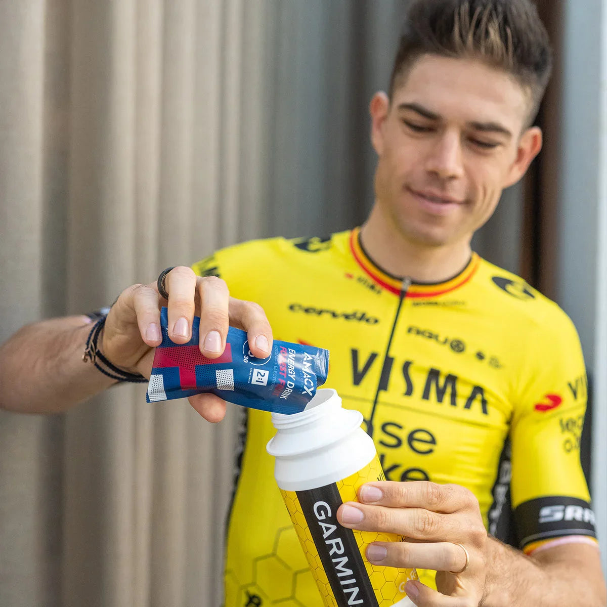 Cyclist in yellow Visma jersey pours energy drink powder into a Garmin sports bottle