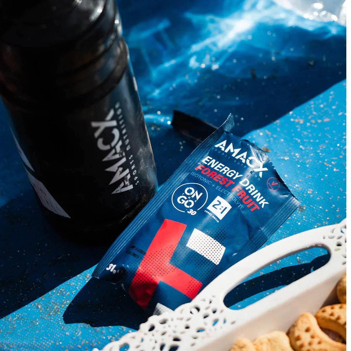 AMACY Energy Drink Forest Fruit packet and black sports bottle on blue surface