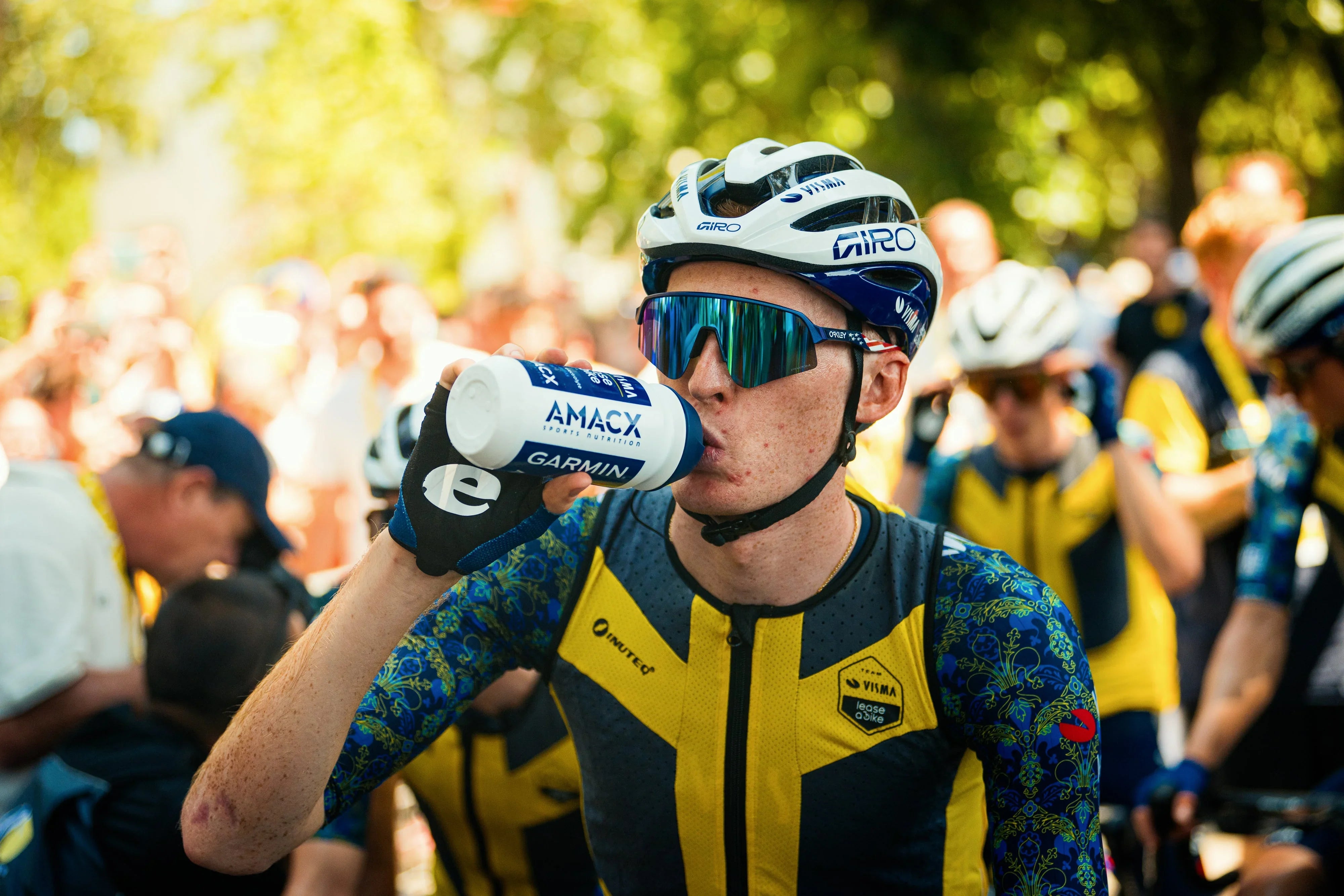 Cyclist in yellow and blue jersey drinking AMACX sports drink during race event