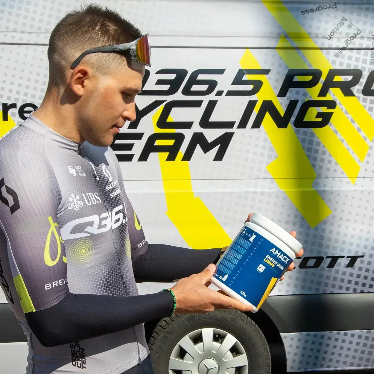 Cyclist holding Amacx Energy Drink container in front of professional cycling team van