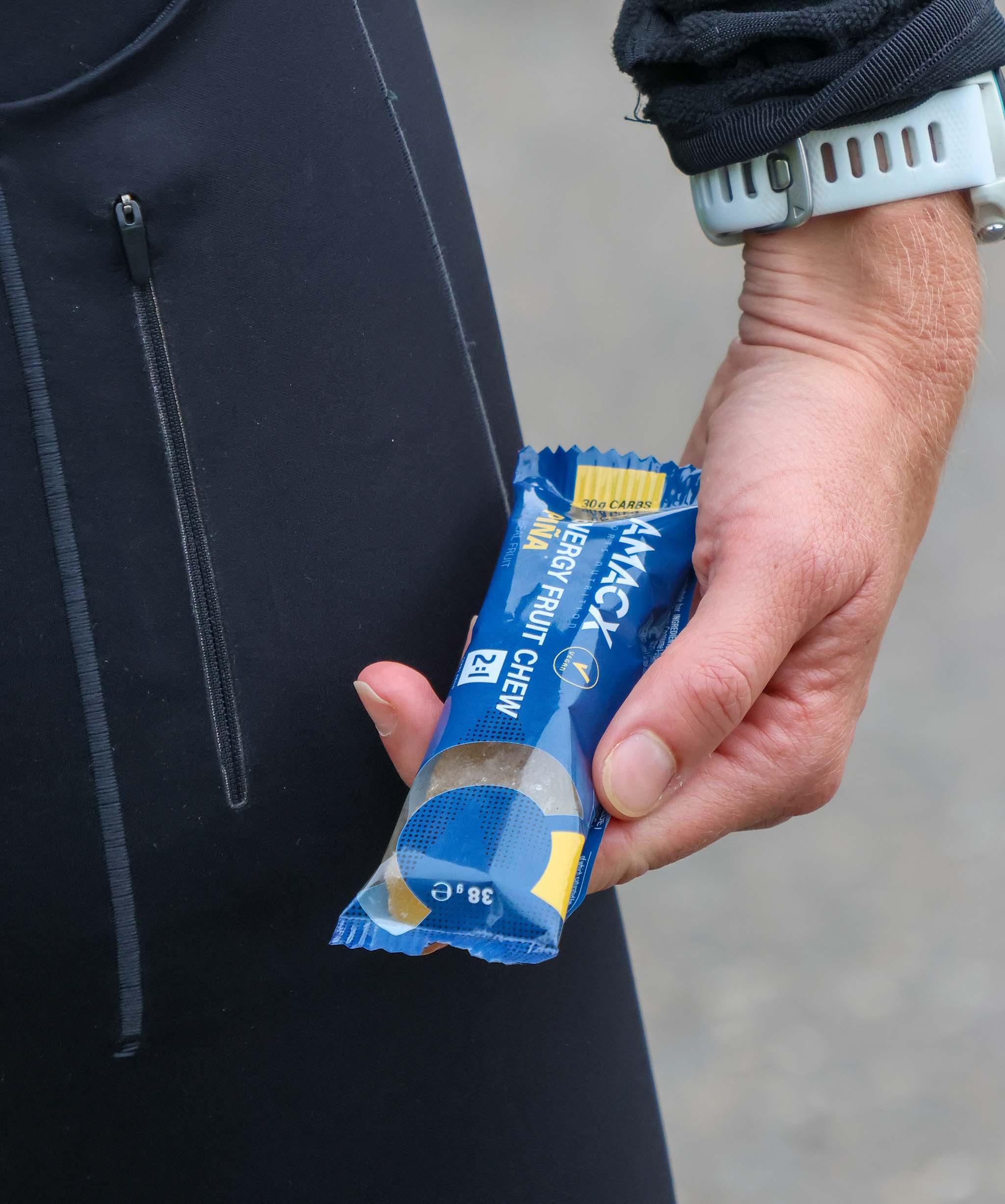 Runner holding Amacx Energy Fruit Chew Piña bar in blue sports packaging outdoors