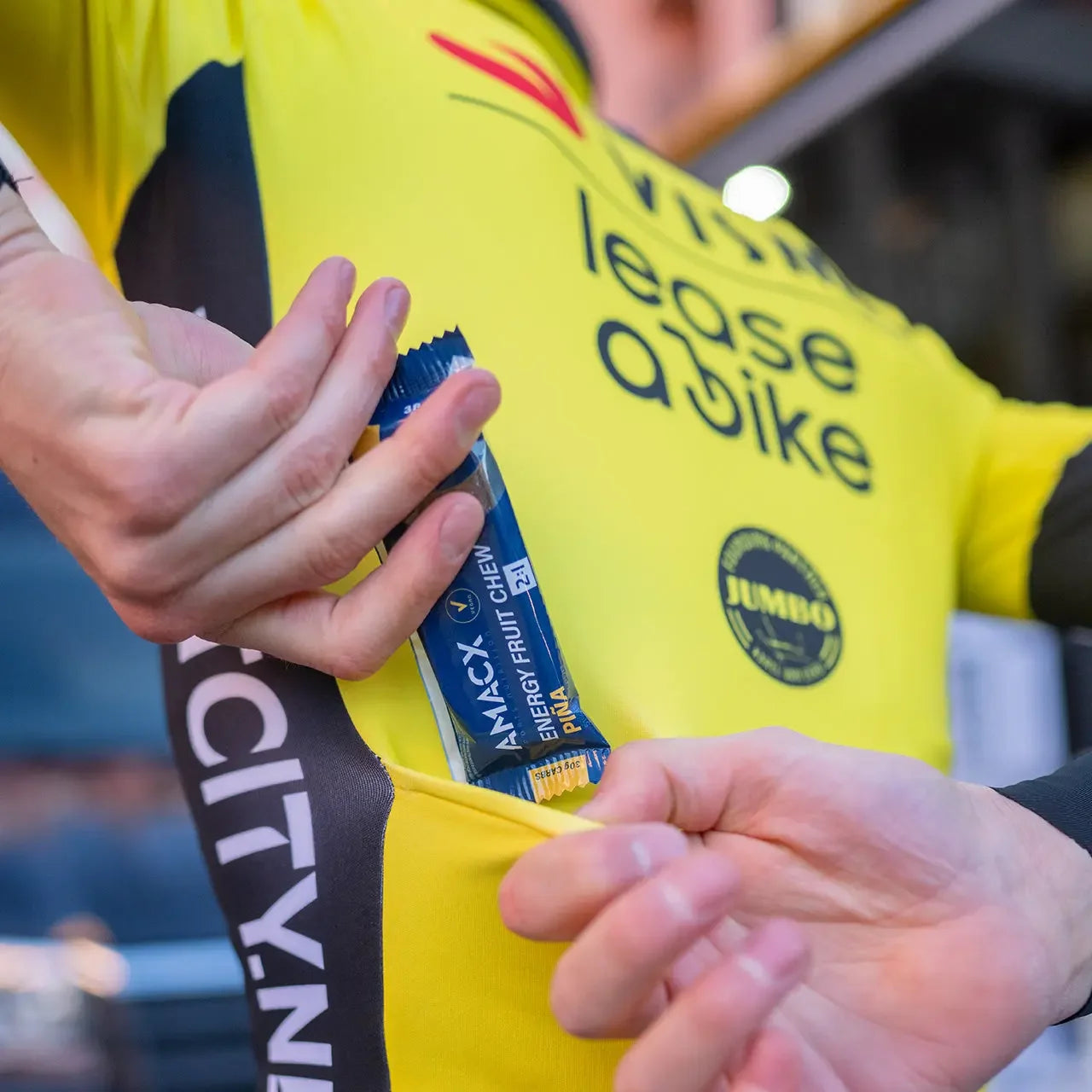 Cyclist in yellow jersey placing Amacx Energy Fruit Chew bar in back pocket