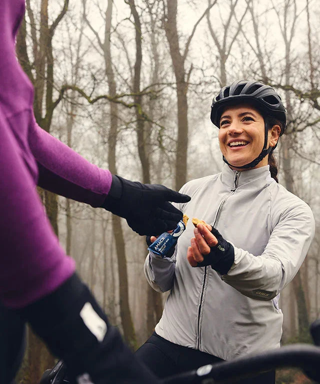 Smiling cyclist in helmet eating oat bar in misty forest, fueling during outdoor ride