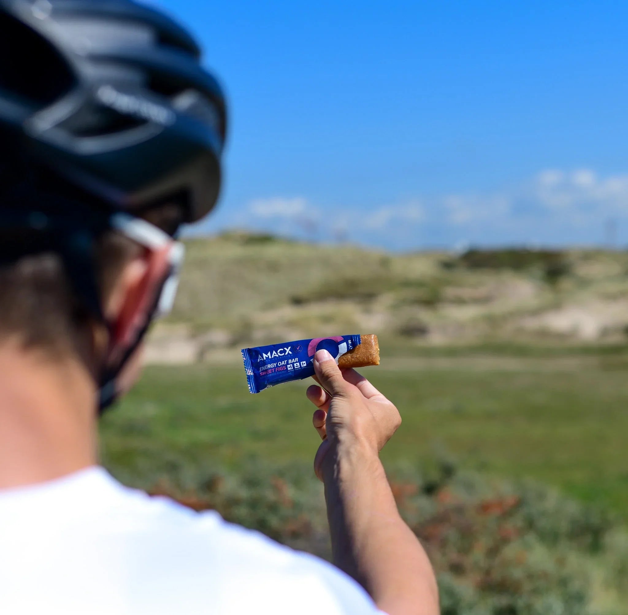 Cyclist holding AMACX energy oat bar outdoors in grassy landscape