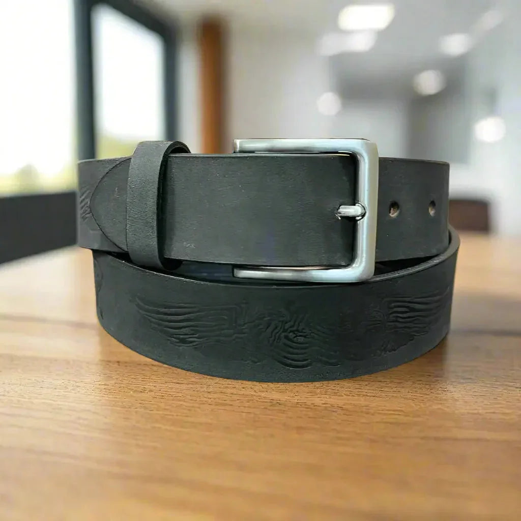 Black leather men's belt with eagle engraving and removable silver buckle on a wooden table