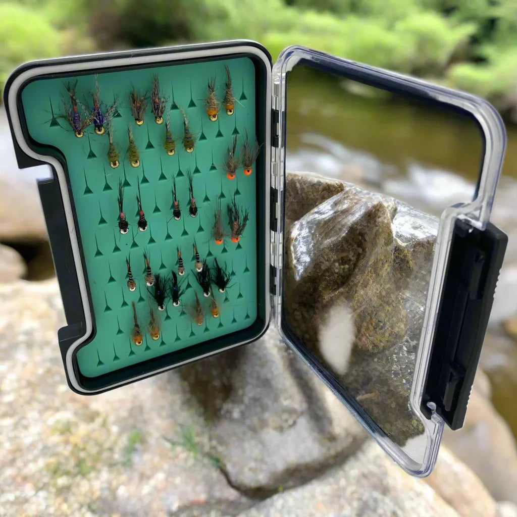 Euro nymph fly fishing kit with assorted flies in open box near a stream