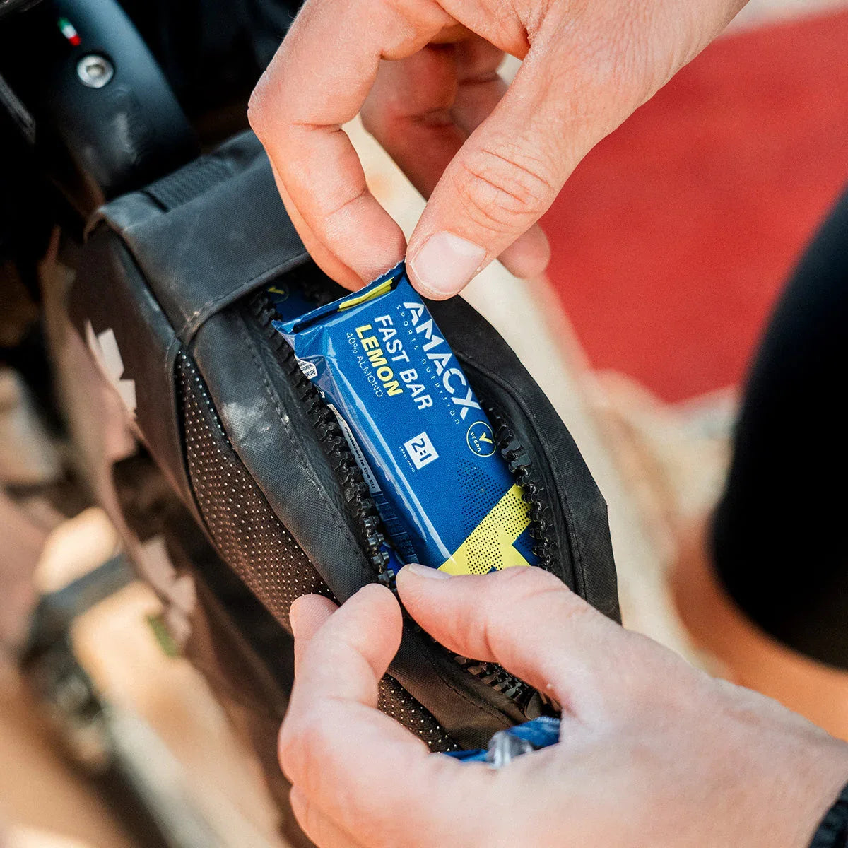 Hand placing AMIX Fast Bar Lemon energy bar in black bike pouch